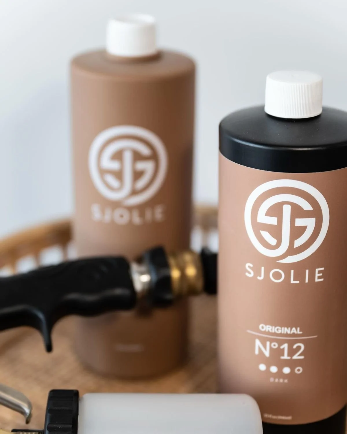 Two bottles of Sjolie product on a wooden tray, with a black tool and other grooming items nearby.