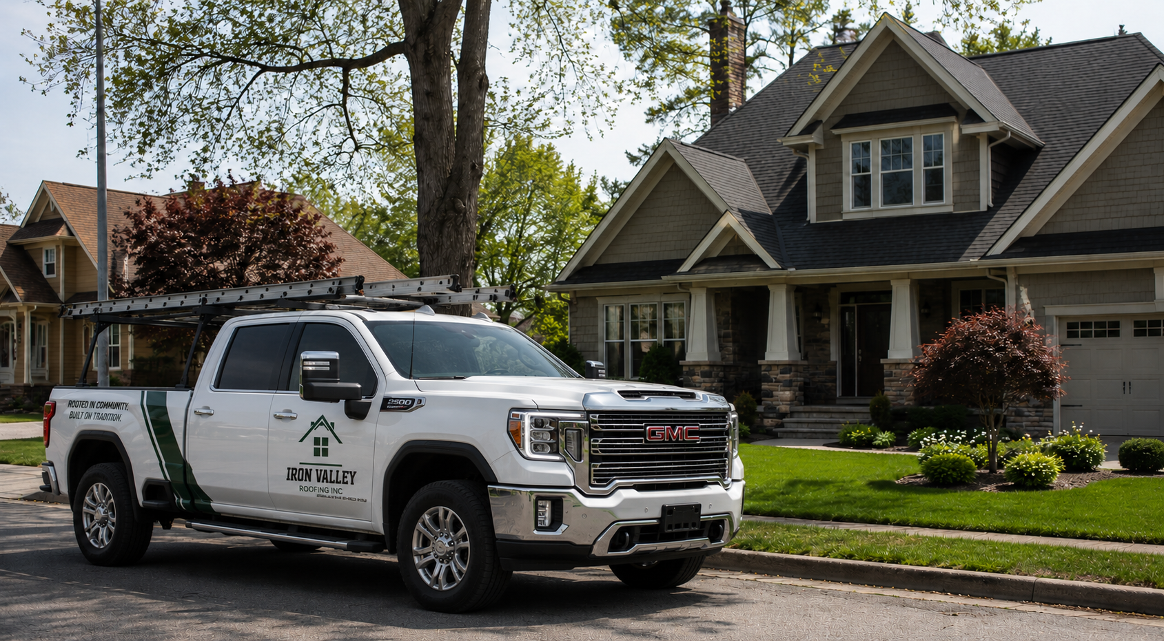 A white GMC crew cab pickup truck with roofing company logo parked in a residential neighborhood with large houses and trees, on a sunny day.