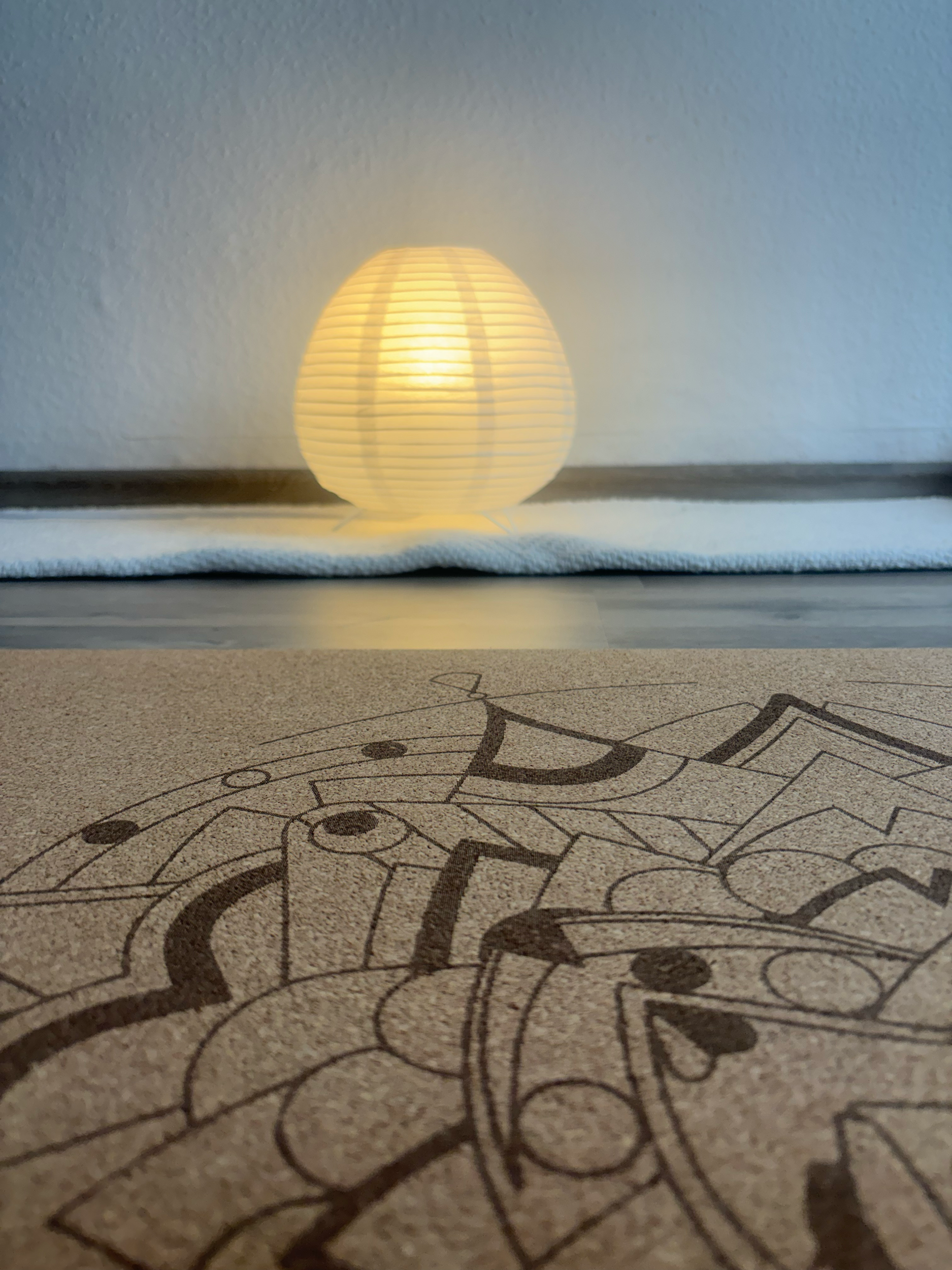 Small, spherical, paper lantern emits warm light, placed on a flat surface next to a yoga mat.