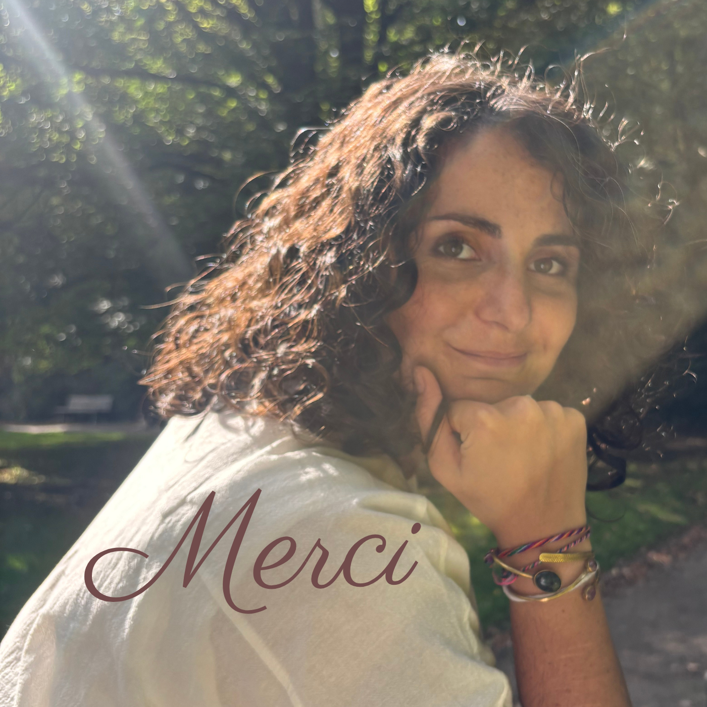 A young woman with curly hair smiling outdoors in sunlight, wearing a white shirt and colorful bracelets, with the word 'Merci' written on the image.