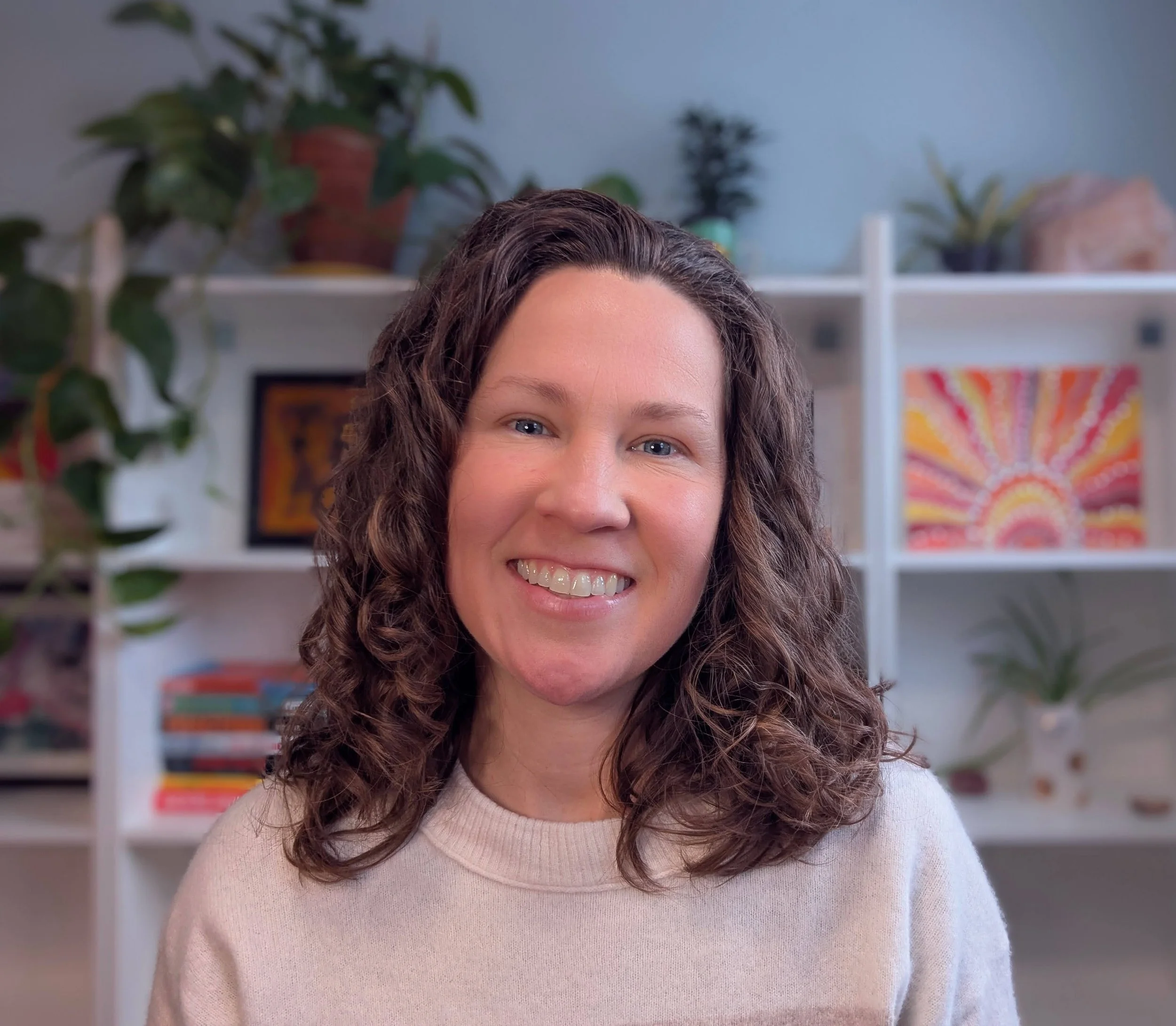 Sara Tatnall, founder of Heart Powered Marketing, smiling in a home office with books, plants, and colourful artwork in the background.