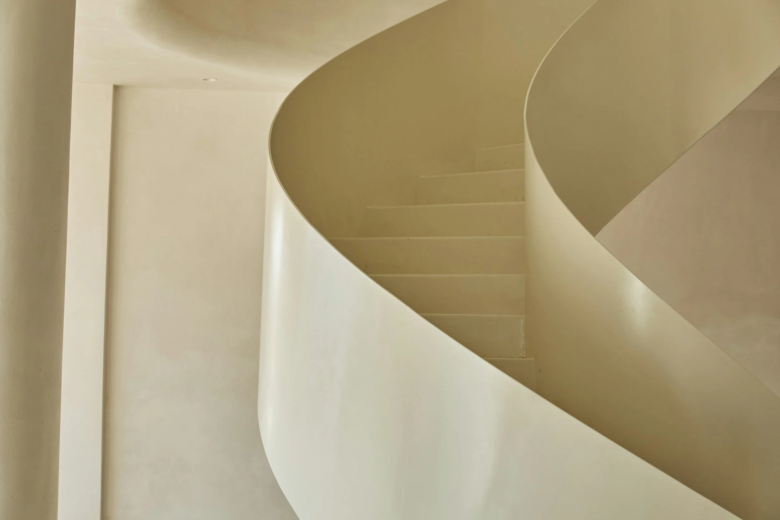 A spiral staircase with beige steps and a matching beige wall in a minimalist interior space.