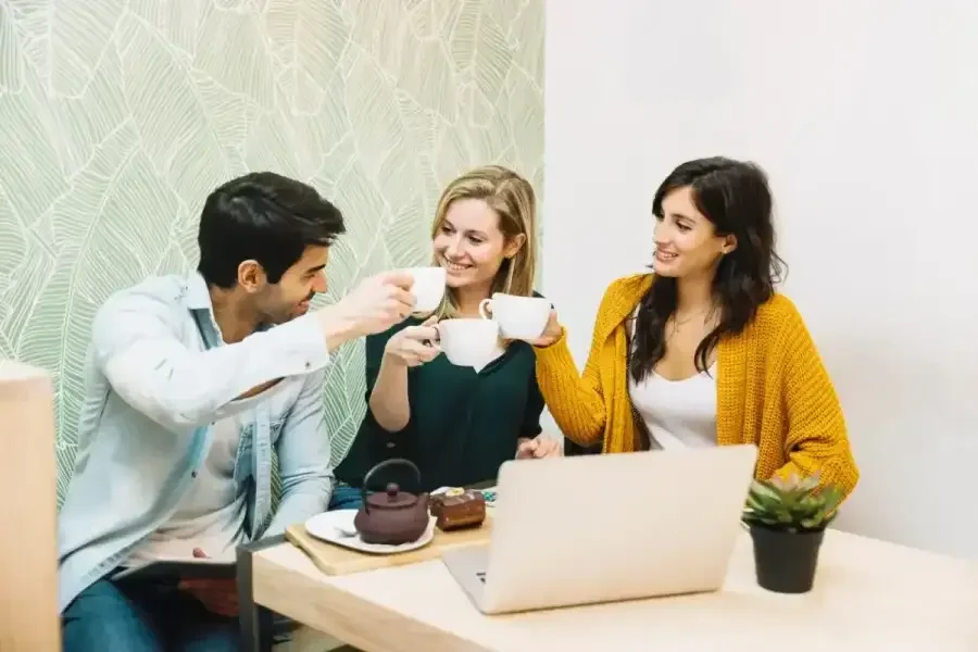 Three colleagues chatting over coffee at a table with a laptop