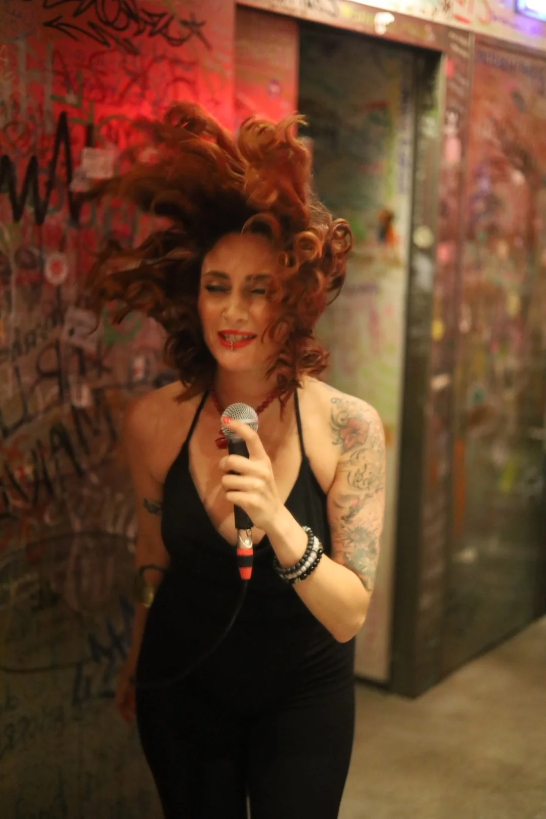 Grace WILDE singing into a microphone in a graffiti-covered room.