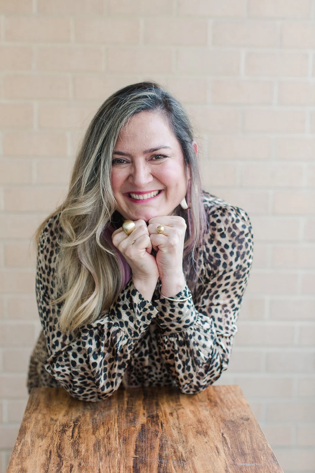 Co-author Claudia Cauterucci, smiling at the camera with her hands under her chin, sitting at a wooden table in front of a brick wall.