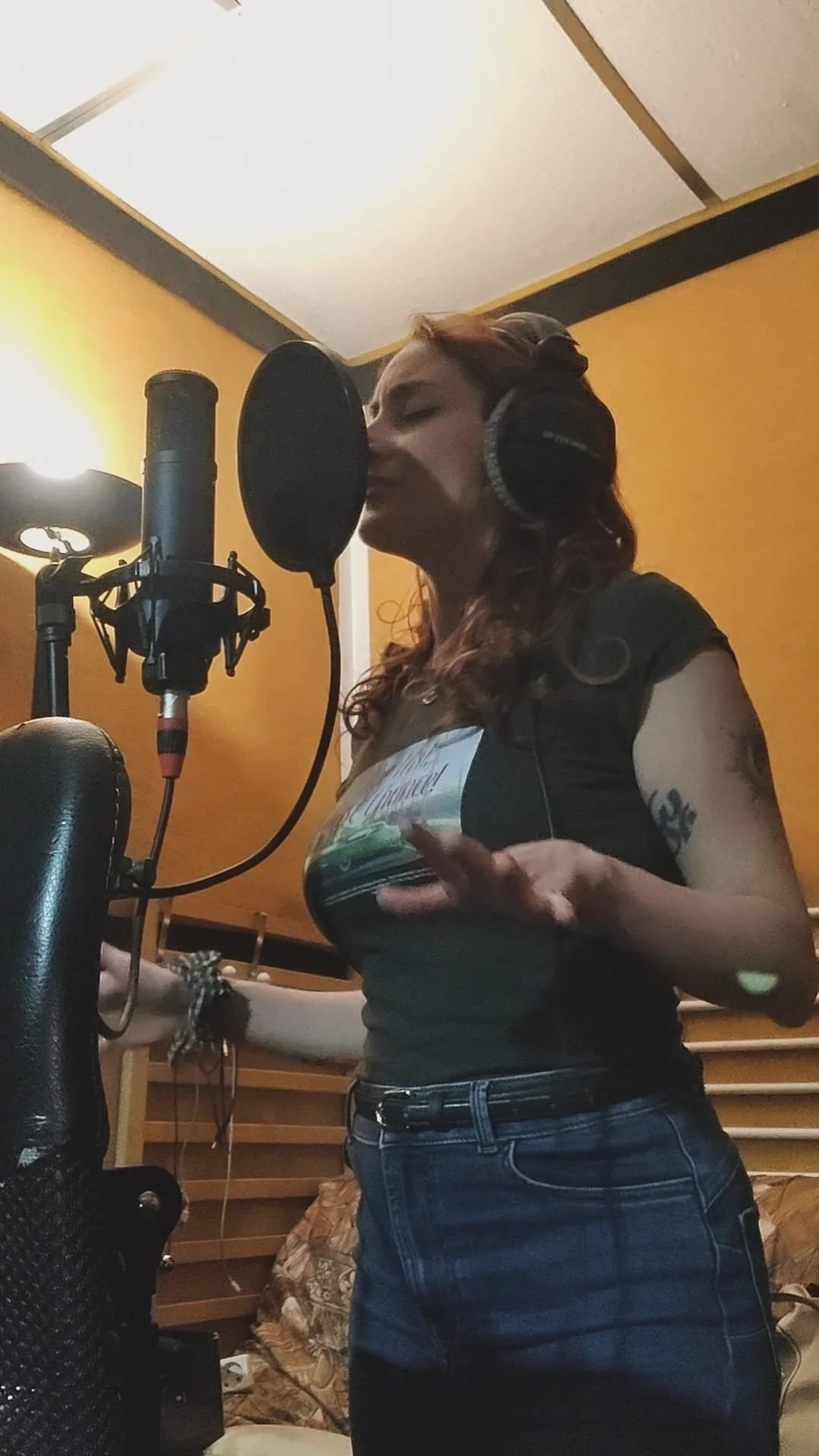 Grace WILDE singing in a recording studio wearing headphones, standing in front of a microphone and a pop filter.