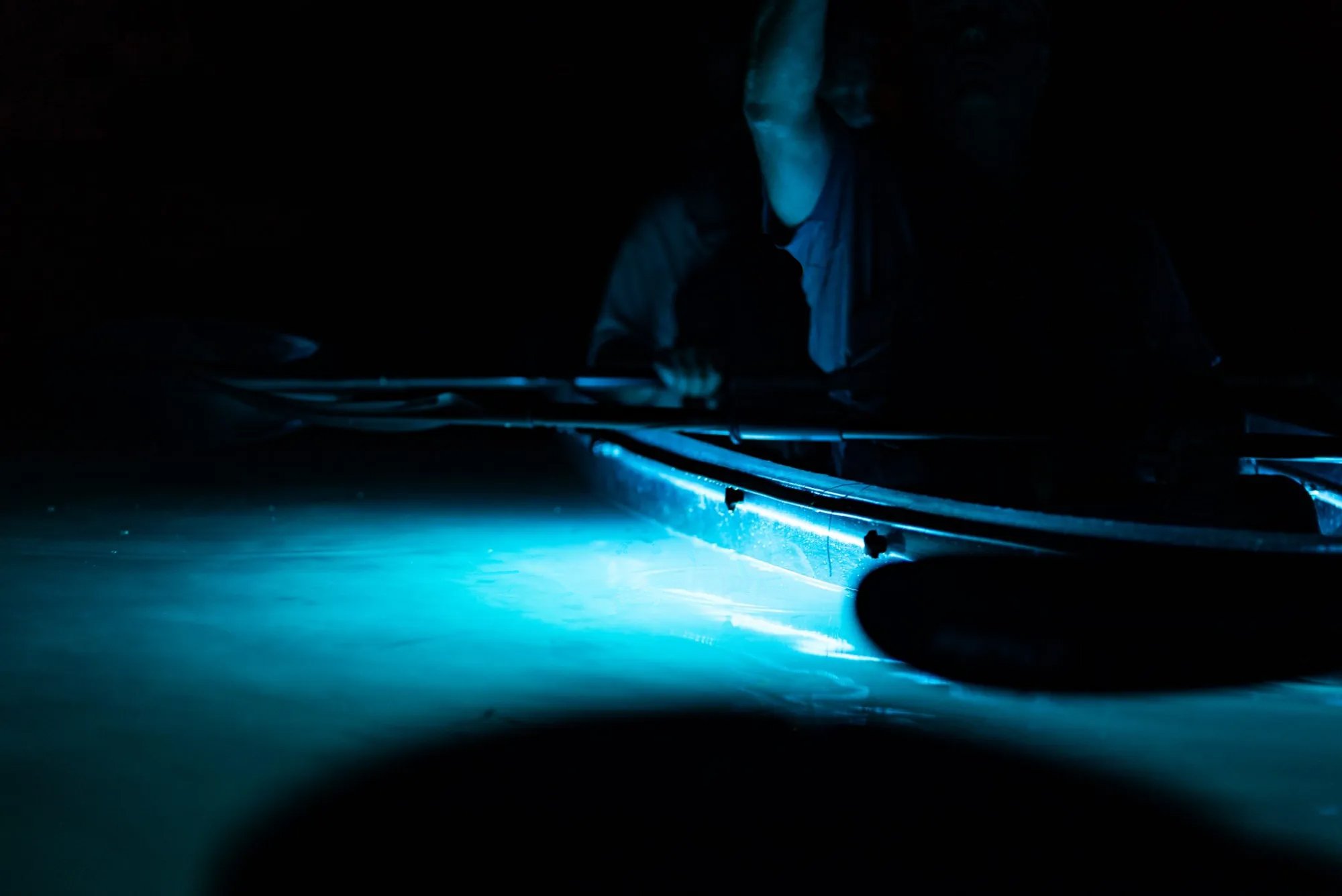 A person working on an aircraft wing at night, illuminated by a blue light, with dark surroundings.