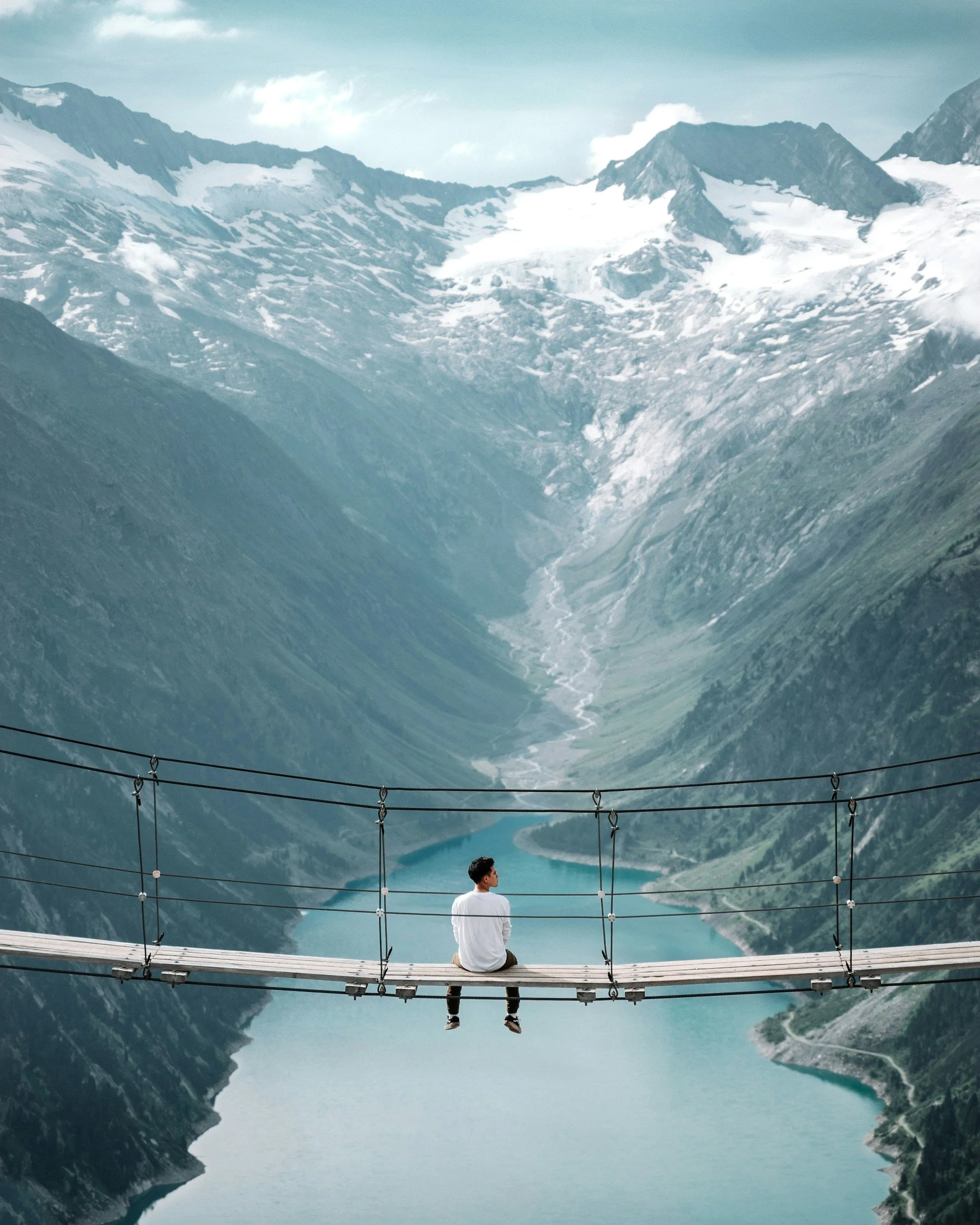 A person sitting on a swinging bridge looking off at a mountain view.