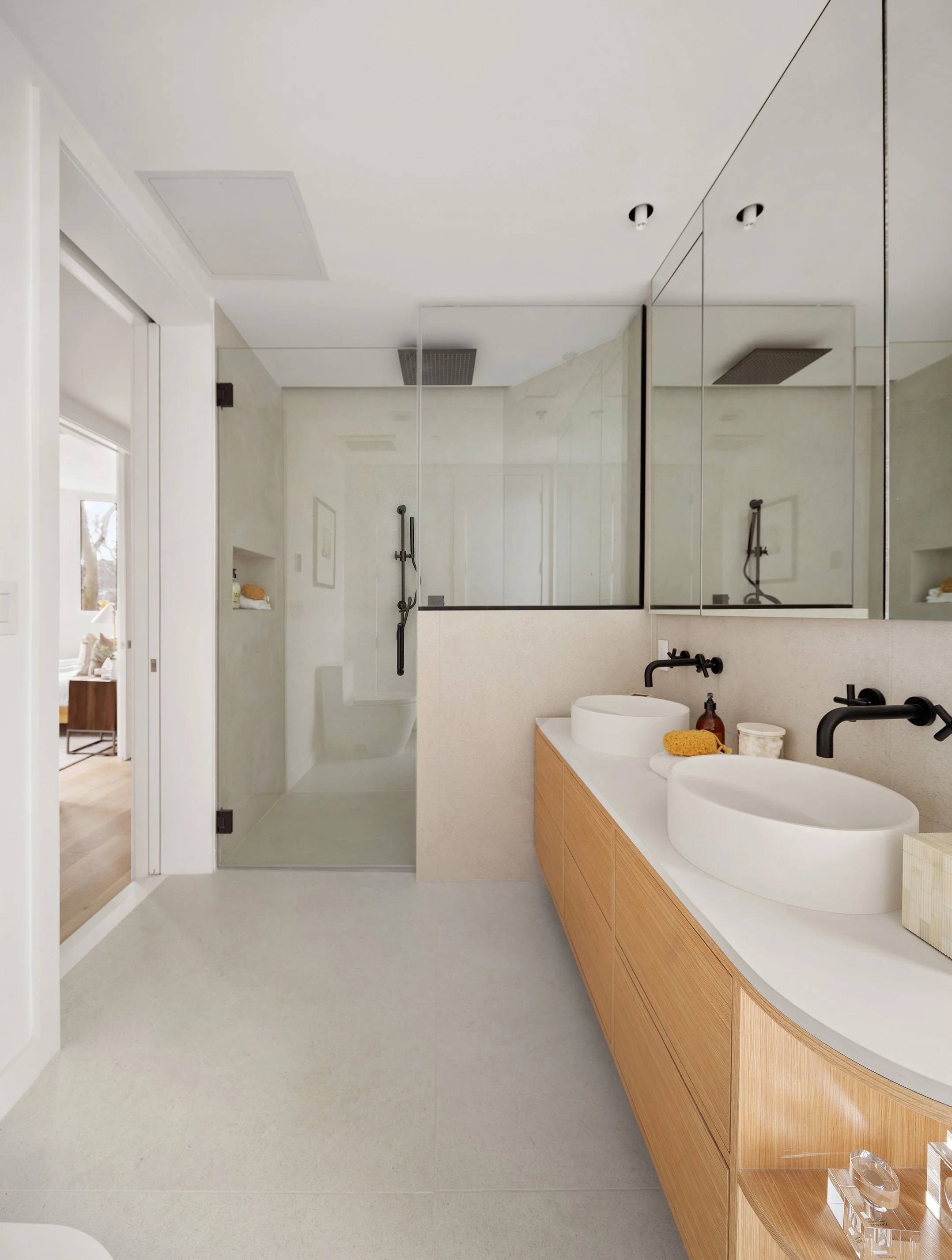 Modern bathroom with dual vessel sinks, black fixtures, wooden cabinet, and glass-enclosed shower with rain shower head.