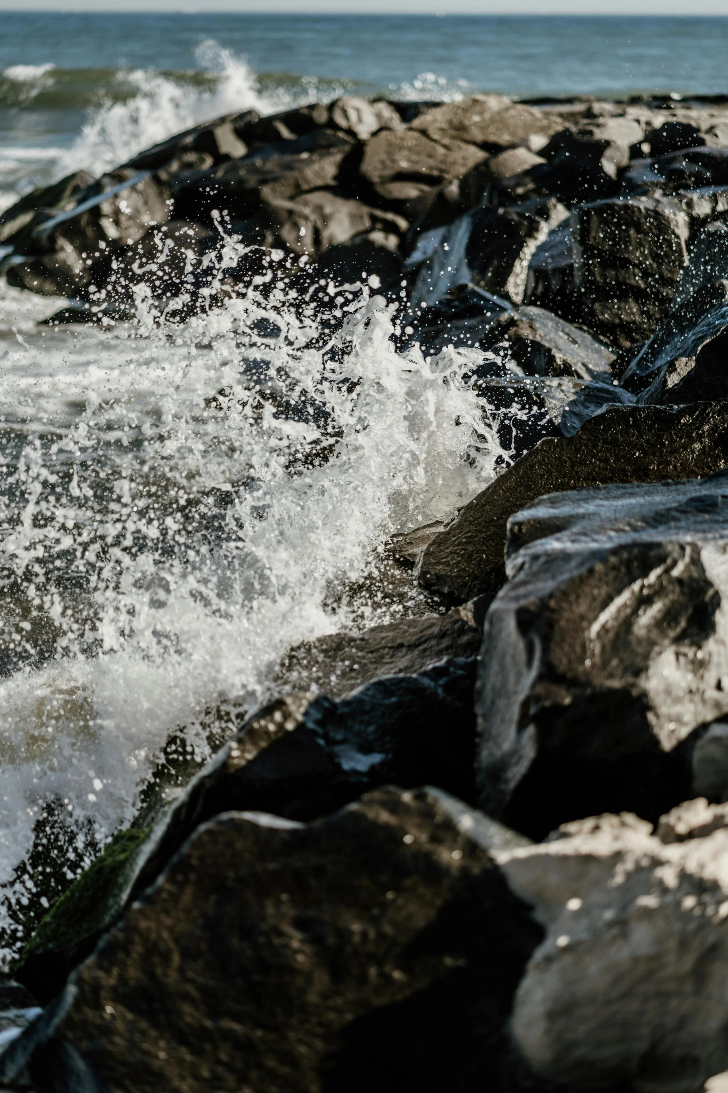 Waves crashing against rocks on the shoreline with the ocean in the background.