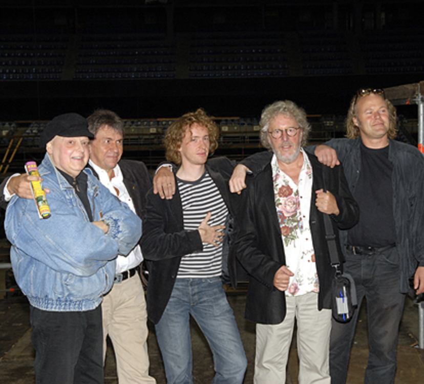 Six men standing together in an indoor venue, casually dressed, posing for a photo.