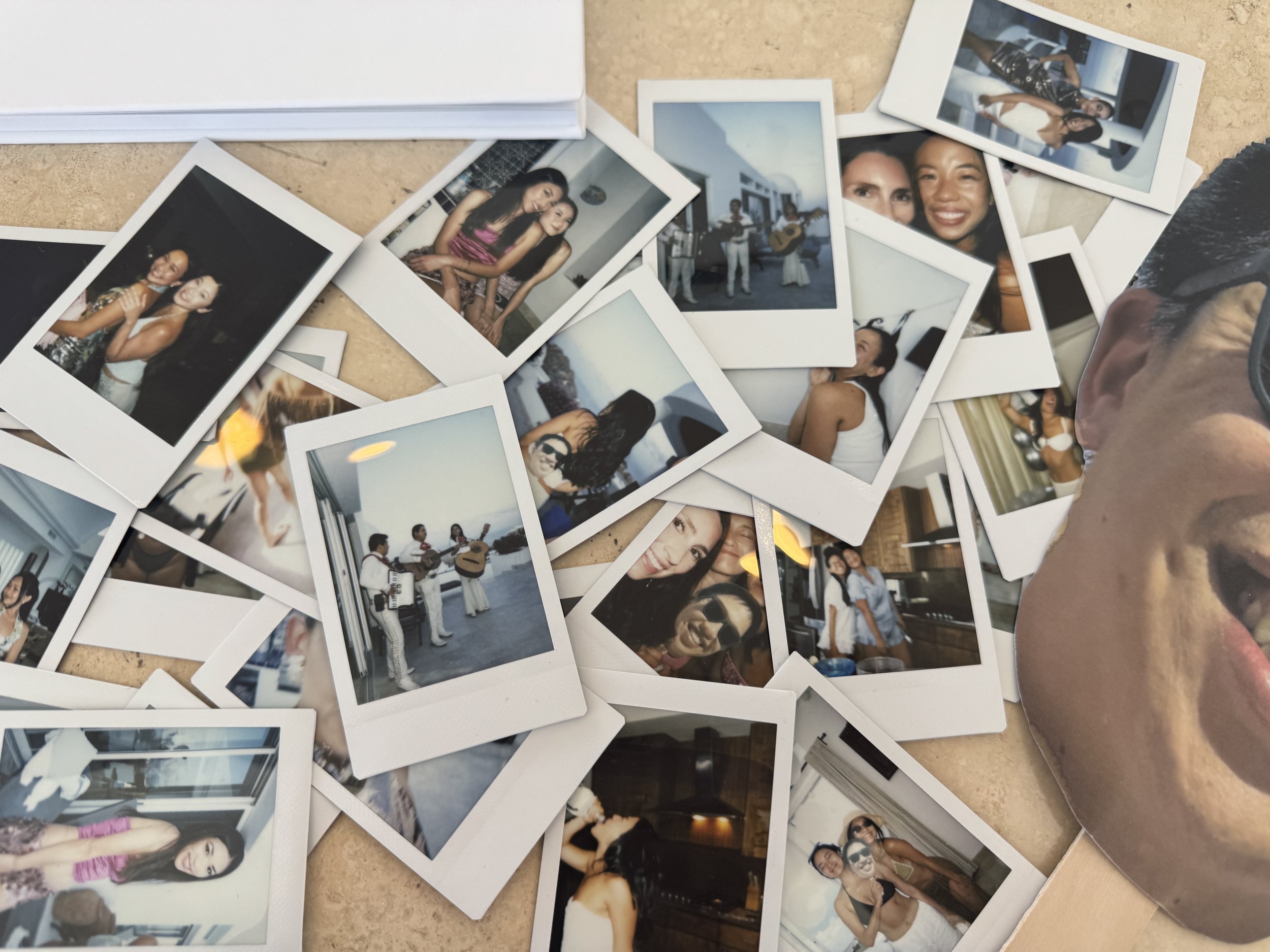 A collection of printed photographs scattered on a table, depicting people at a social gathering with some playing musical instruments and others posing for the camera.