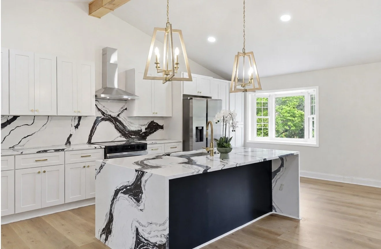 Modern kitchen with white cabinets, a marble island, a stainless steel refrigerator, gold fixtures, and black and white marble backsplash
