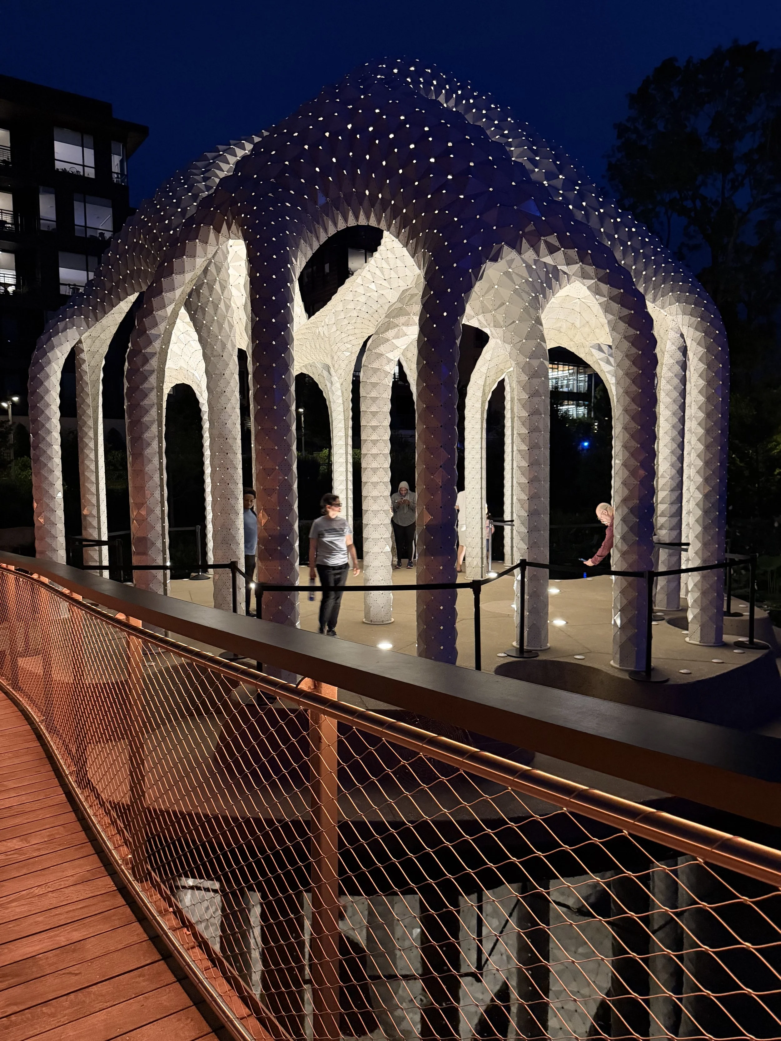 Visitors walking through the illuminated public art pavilion at Downtown Cary Park in Cary, North Carolina, at night.