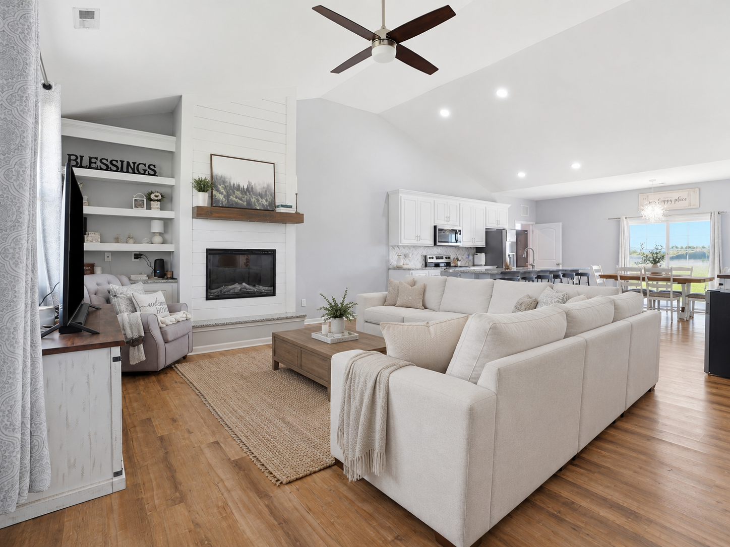 Open-concept living room with vaulted ceilings, fireplace, light-colored sectional, and adjoining kitchen in a Bailey, North Carolina home.