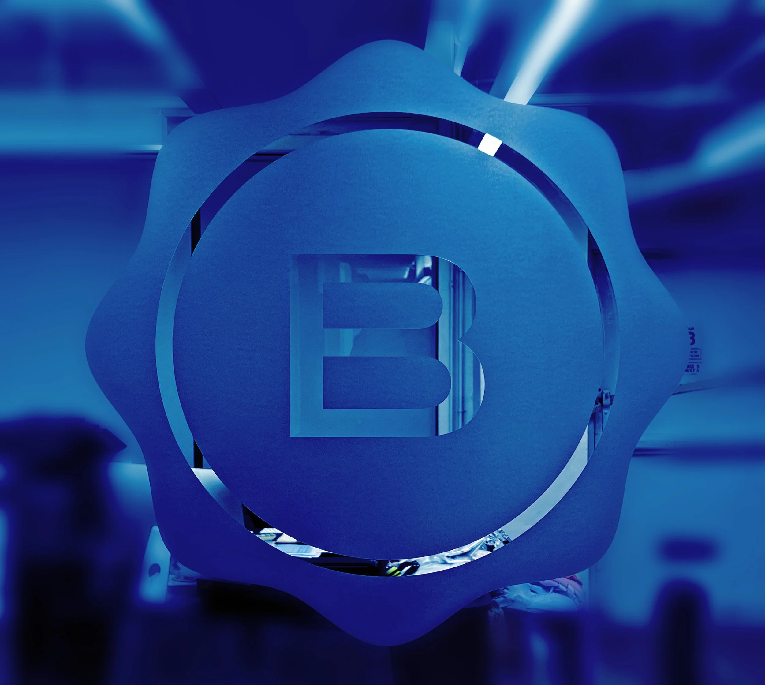 A large, abstract, blue-colored sculpture with illuminated light streaks surrounding it, located in an indoor space with a modern, futuristic design.