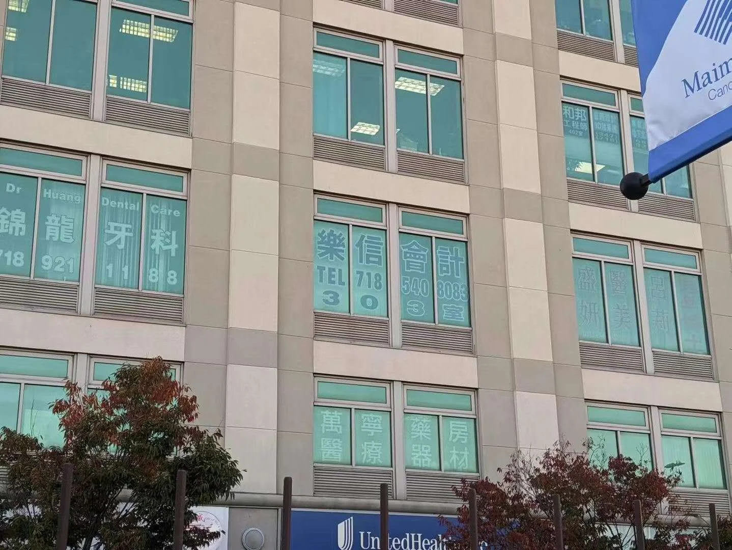 Windows with blue signs and white text in Chinese and English, advertising dental care, accounting, and medical supplies, on a beige multi-story office building.
