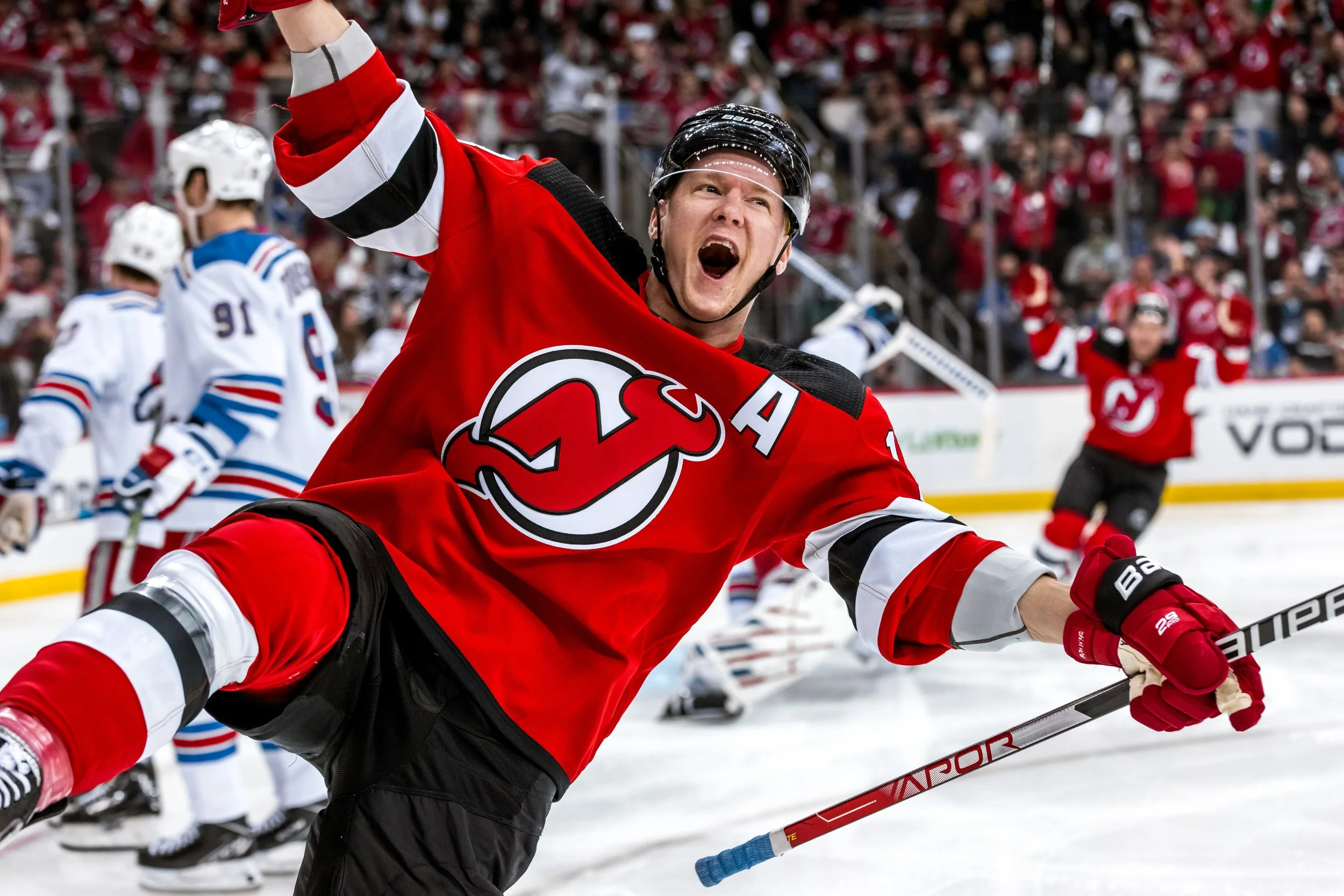 Hockey player in red jersey celebrating on ice rink with fans in background.