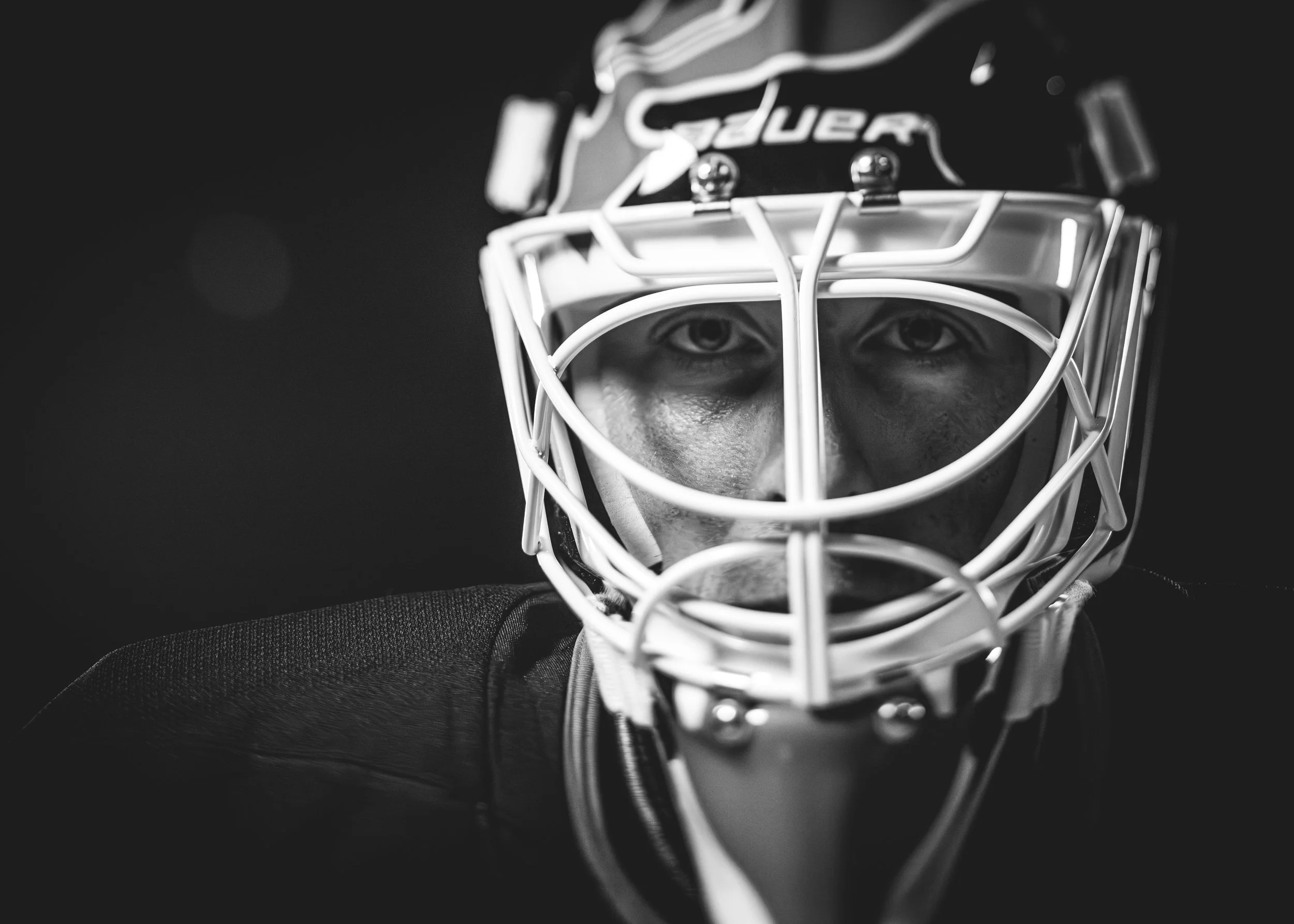 Close-up black-and-white photograph of a hockey goalie wearing a mask and protective gear.