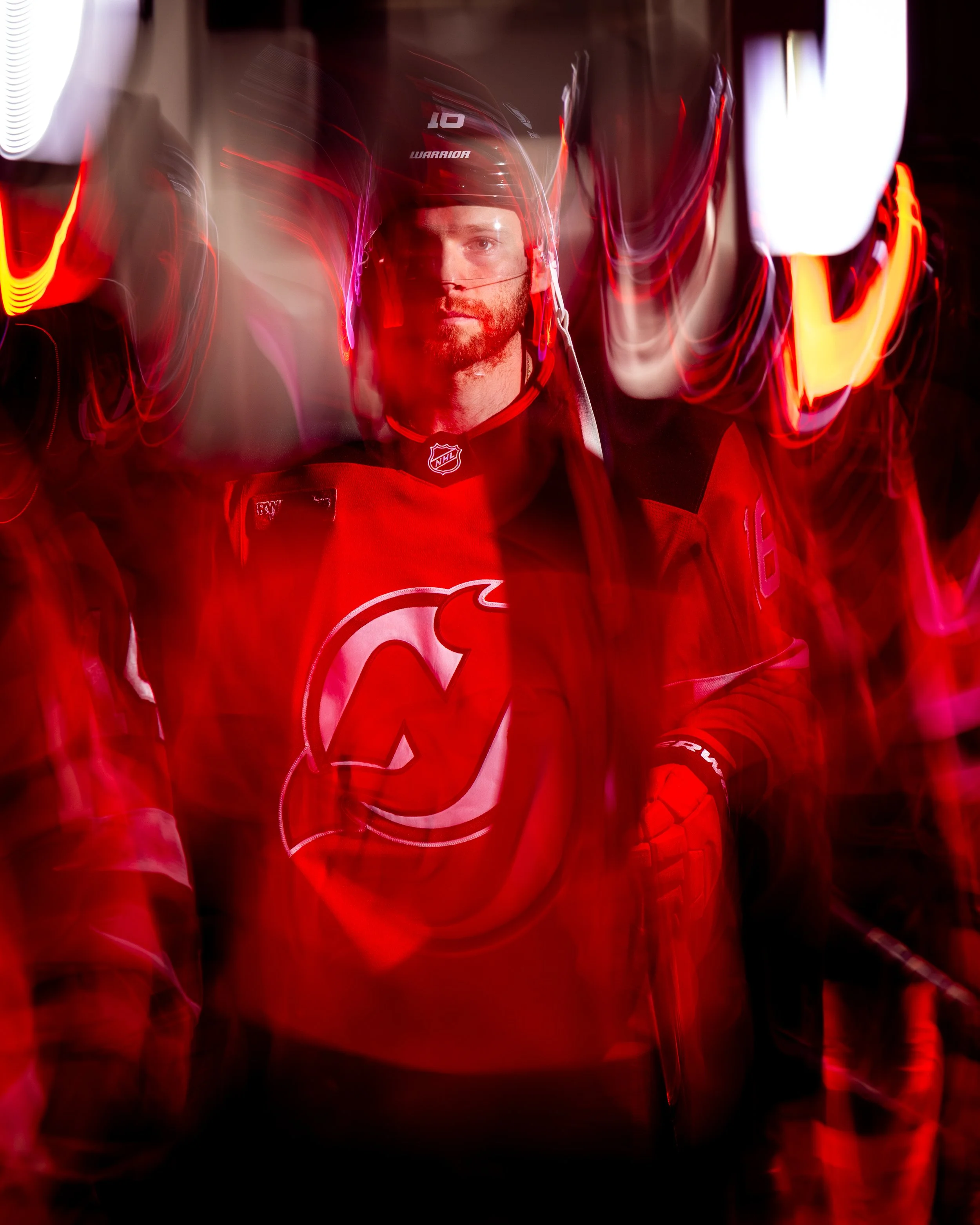 Reflected image of a hockey player in red uniform and helmet, illuminated with red and yellow lights, with the player's face visible through the reflection.