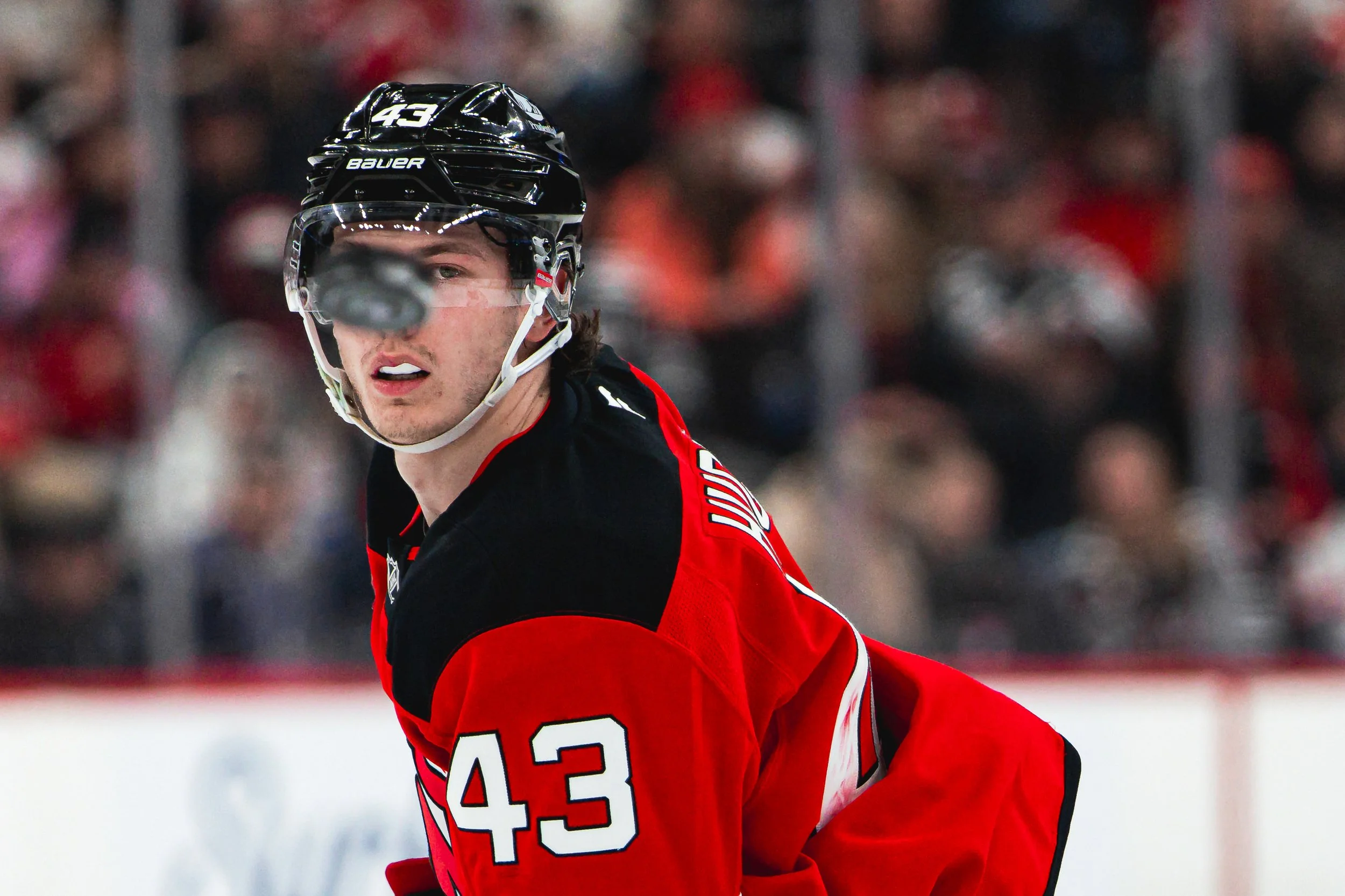 A hockey player in a red and black jersey with the number 43 on his helmet and jersey, wearing a black helmet with a clear visor, is on the ice during a game.