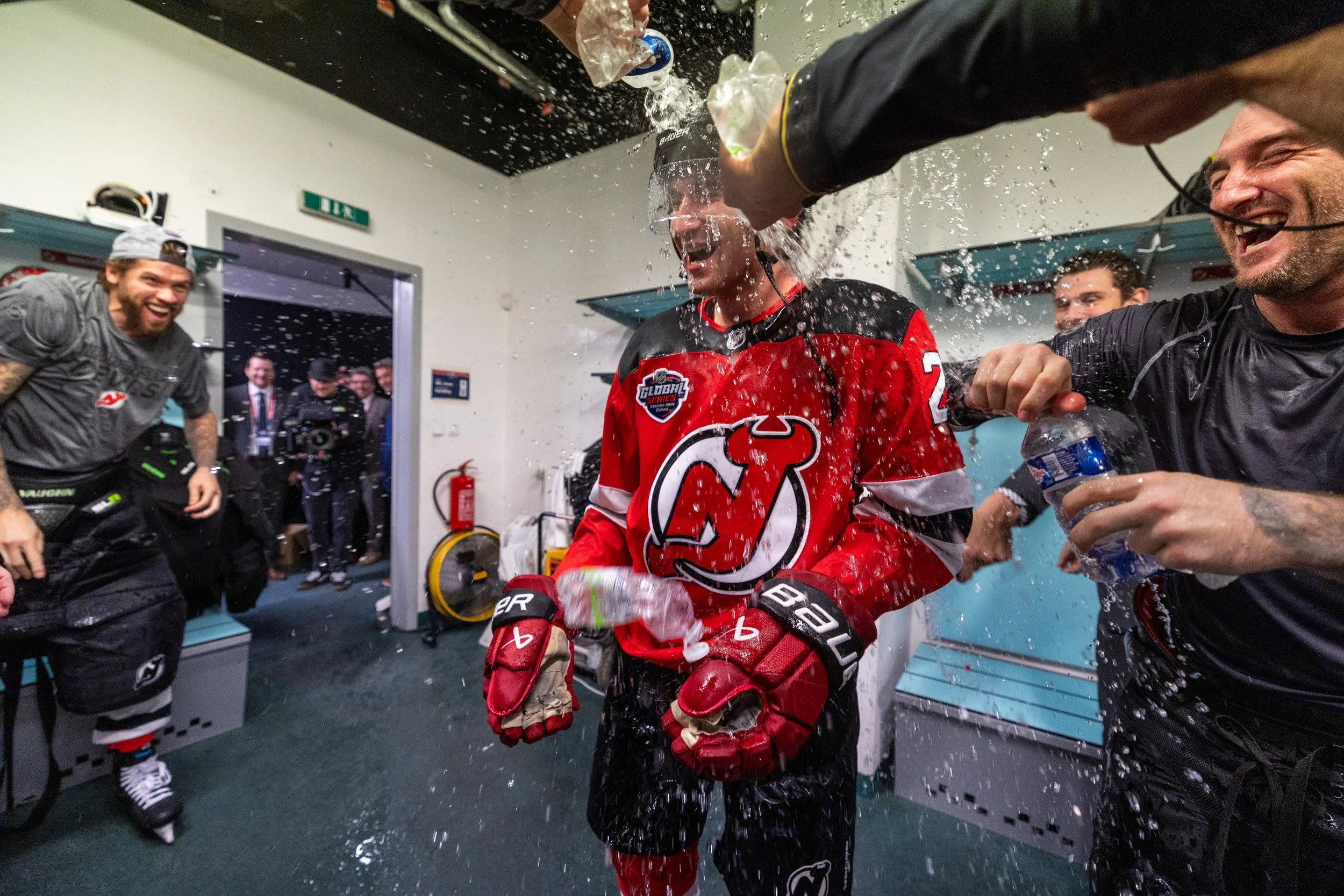 Hockey player celebrating in locker room with teammates, water splashing around.