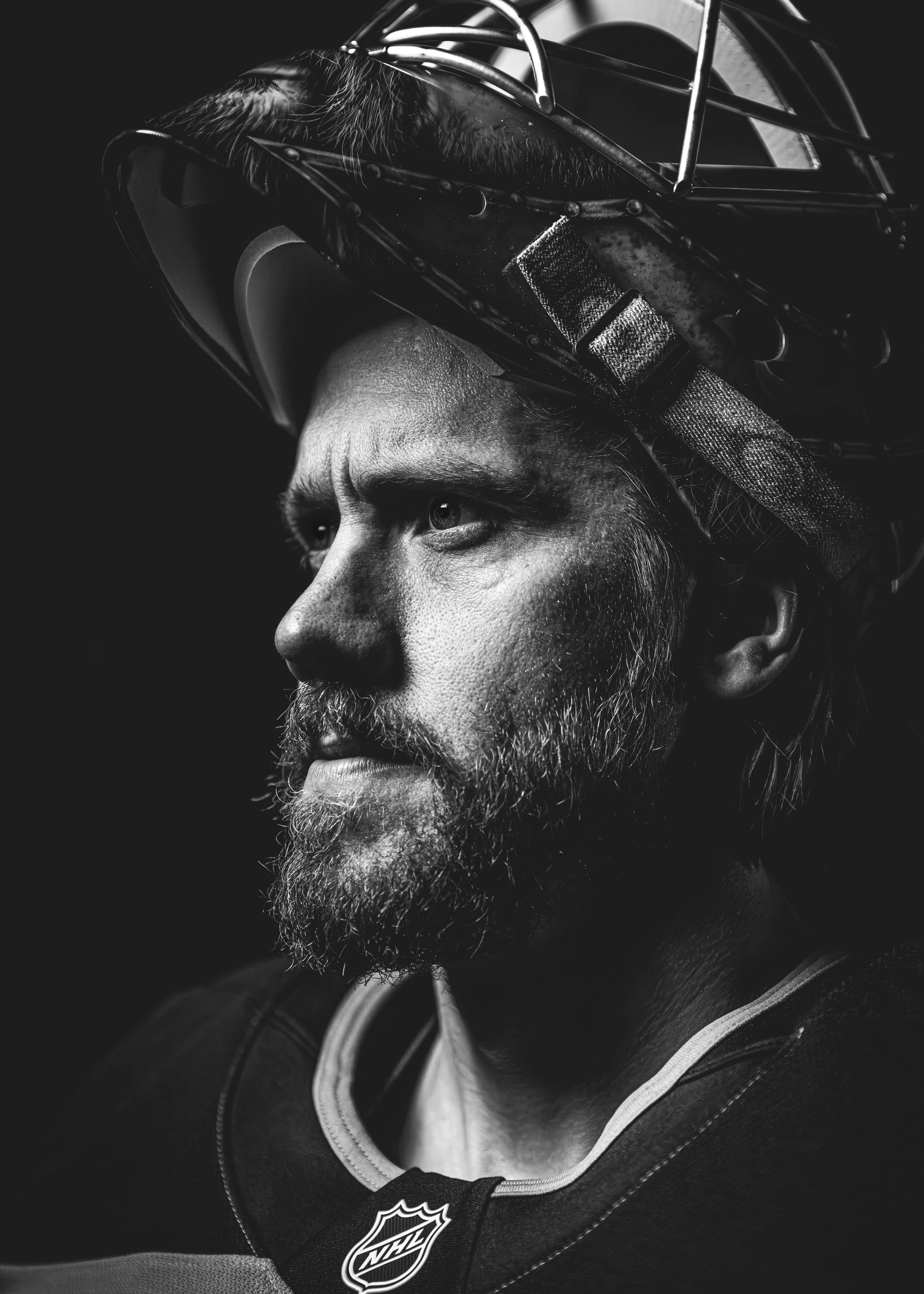 Close-up black and white portrait of a male ice hockey player wearing a helmet and jersey with the NHL logo.