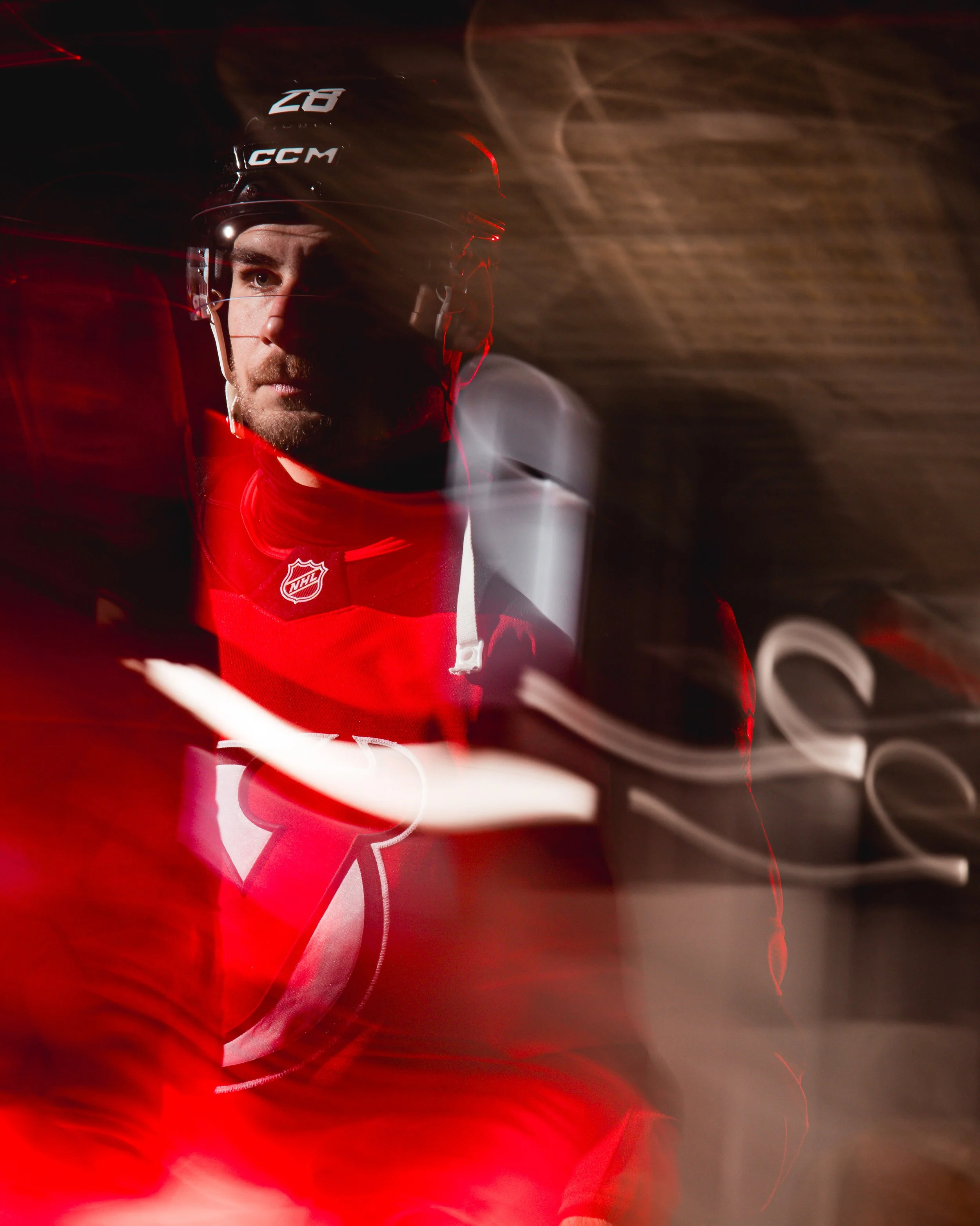 A hockey player wearing a black helmet with the CCM logo and a red jersey with a white NHL logo, looking intensely forward, with motion blur effects and swirling lights around.