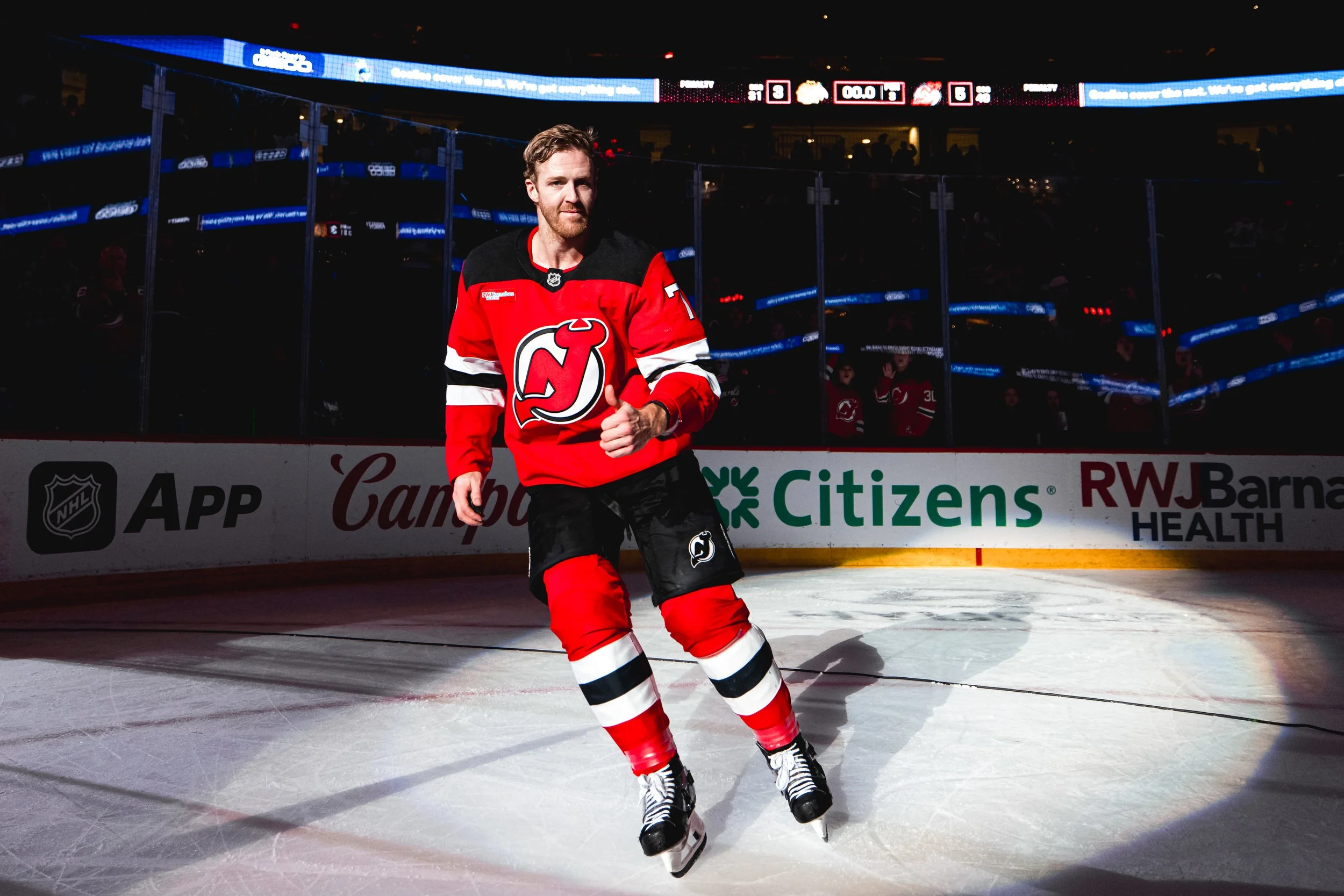 A male ice hockey player in a red and black uniform skating on the ice rink after a game.