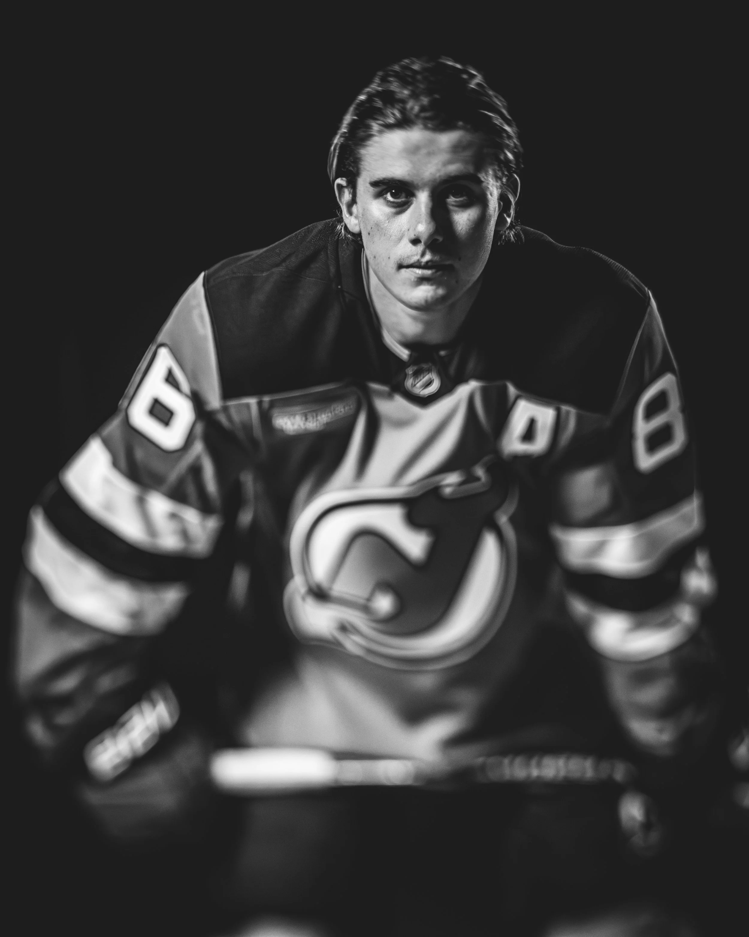 A black and white close-up photo of a young male hockey player in gear, with a serious expression, looking directly at the camera.
