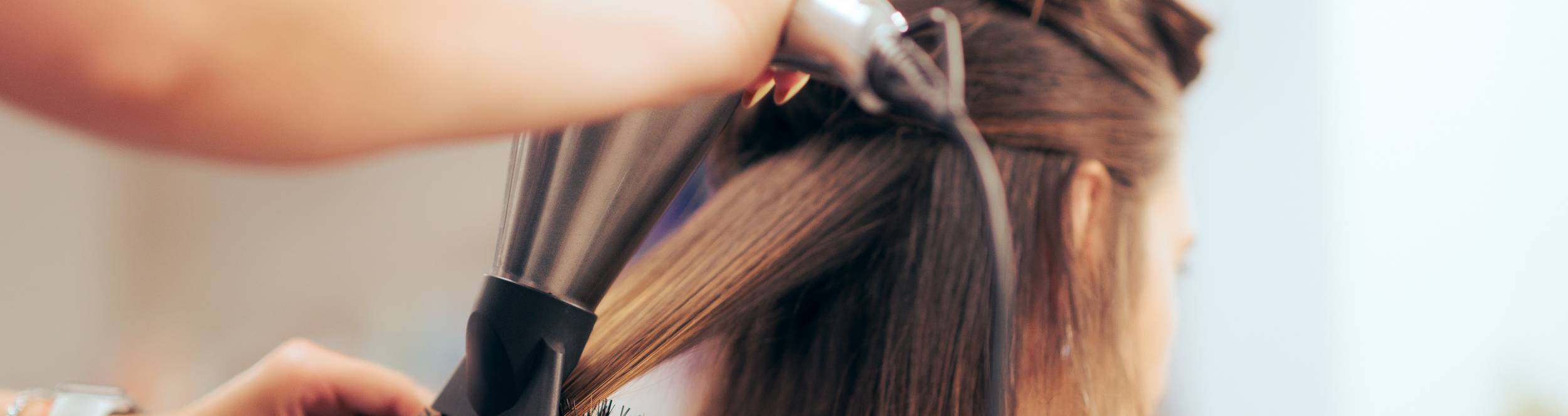 A person with brown hair using a curling iron to curl hair.