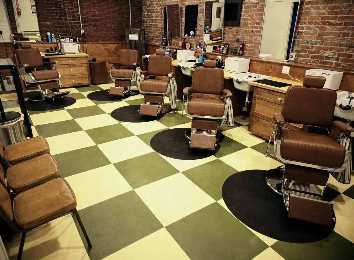 Barber shop with three barber chairs, mirrors, and workstations, featuring a yellow and green checkered floor and brick walls.