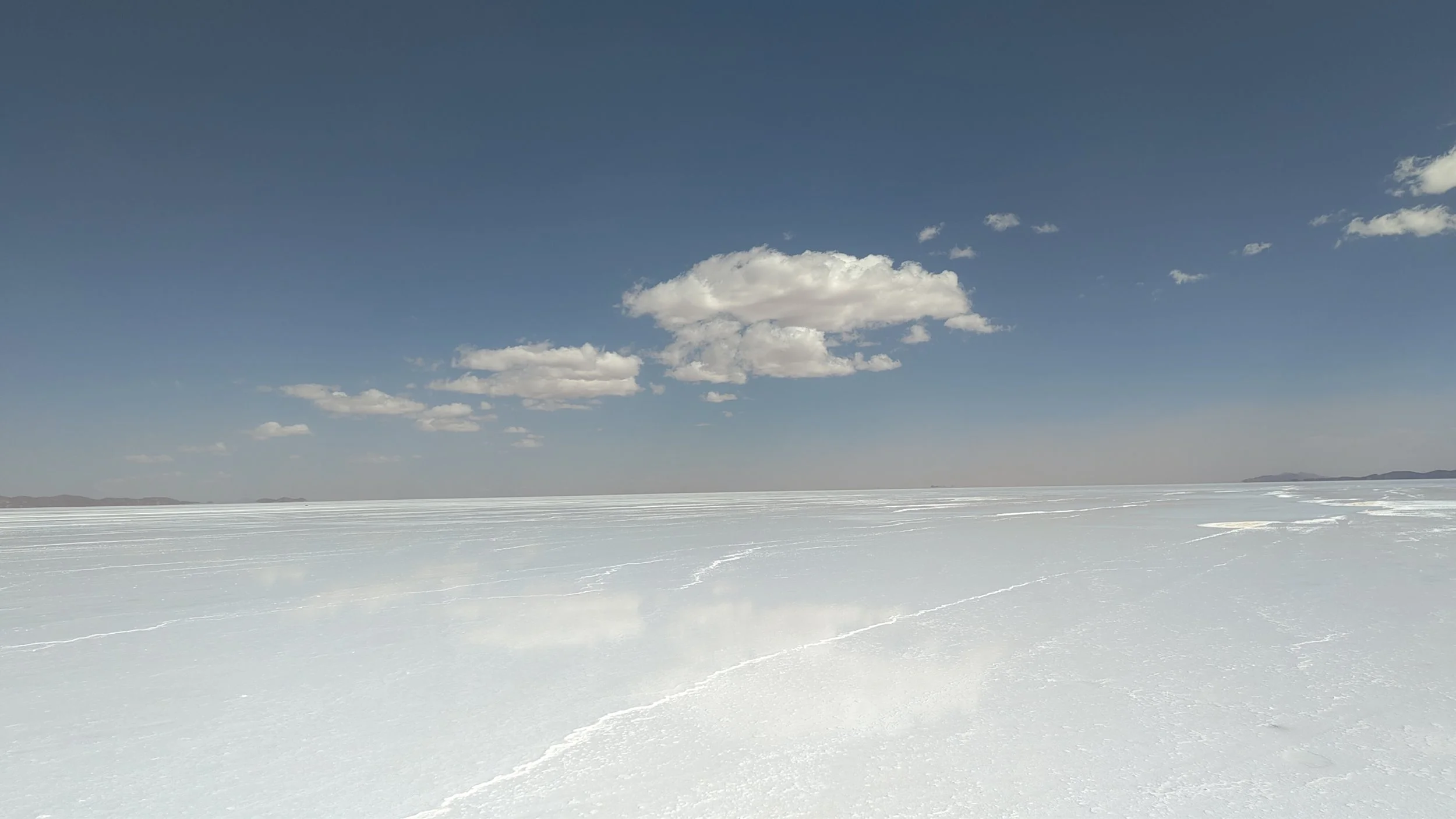 Weiße salzige Ebene unter einem blauen Himmel mit wenigen Wolken.