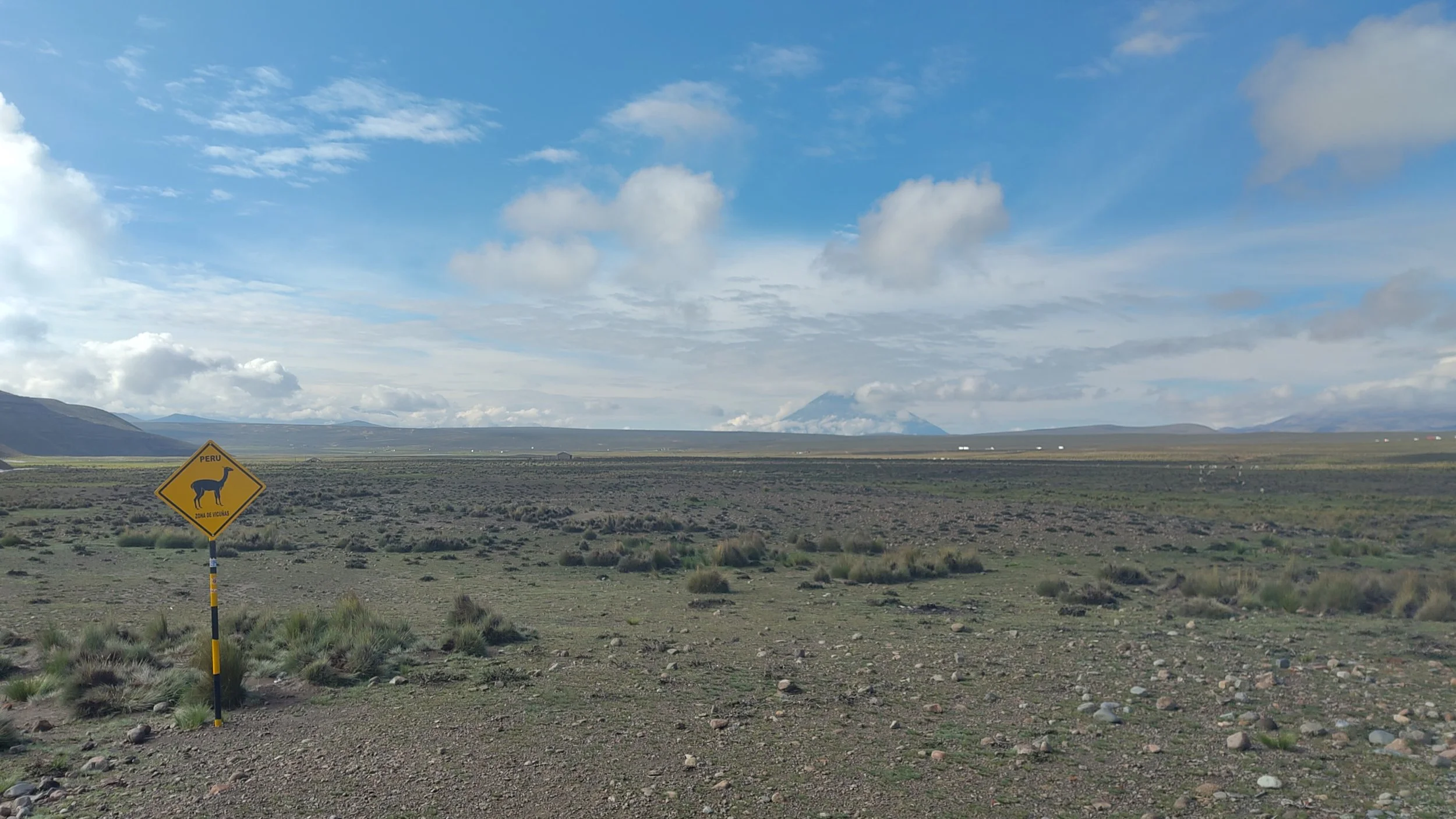 Landschaft in Peru mit einem Straßenverkehrsschild, das einen Guanakon zeigt.