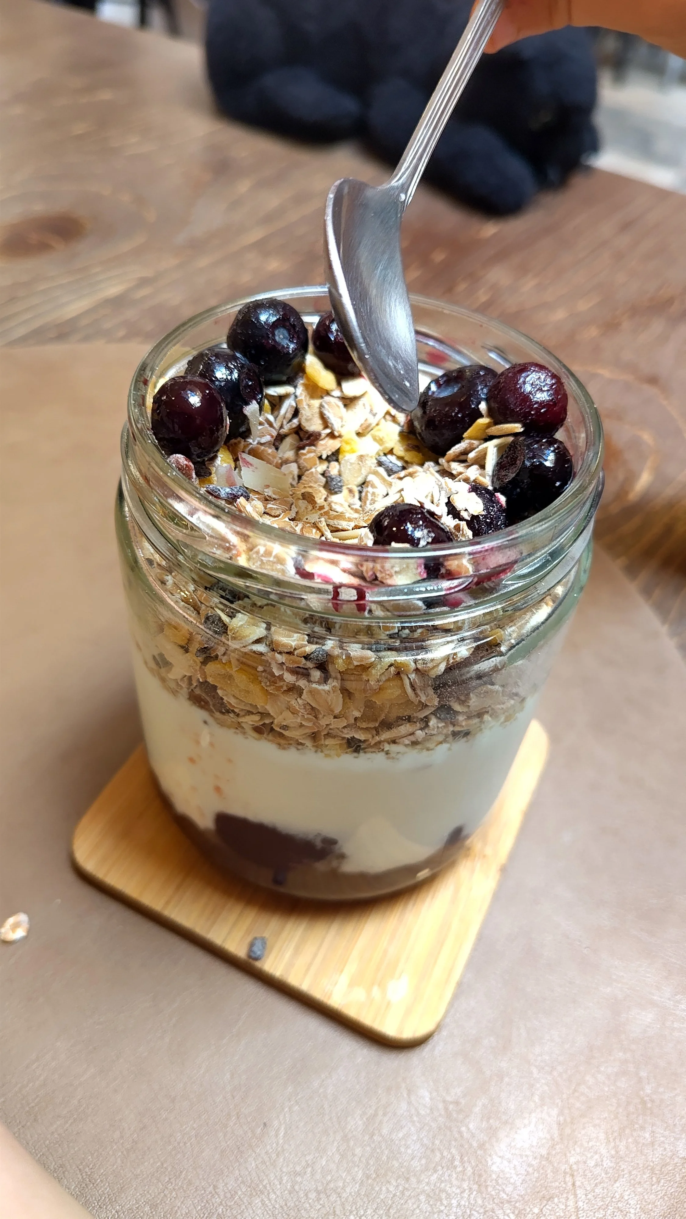Ein Glas mit Joghurt, Granola, Blaubeeren und Schokolade auf einem Holzteller
