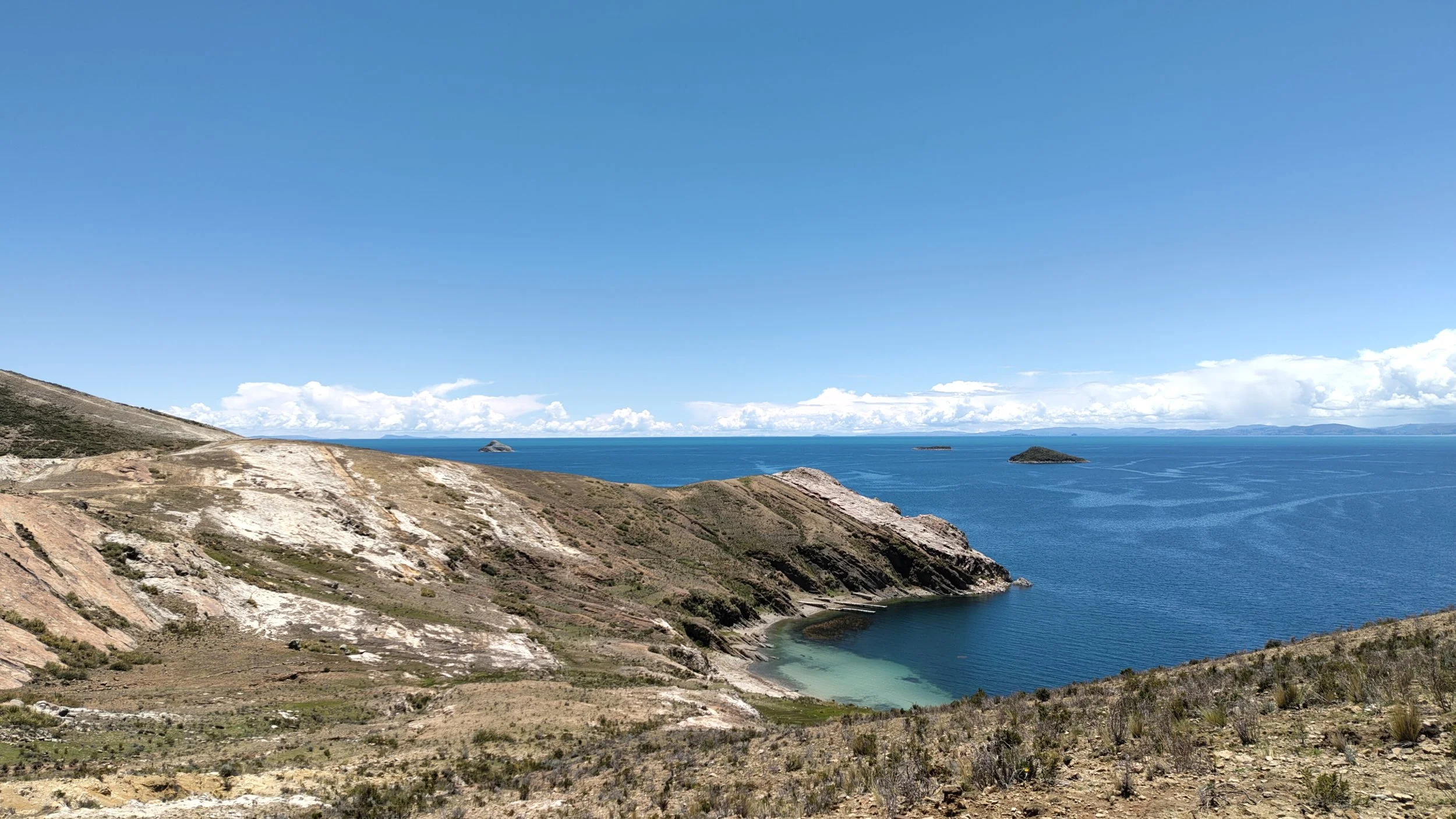 Blick auf eine Küstenlandschaft mit Bergen und Meer unter klarem blauen Himmel.