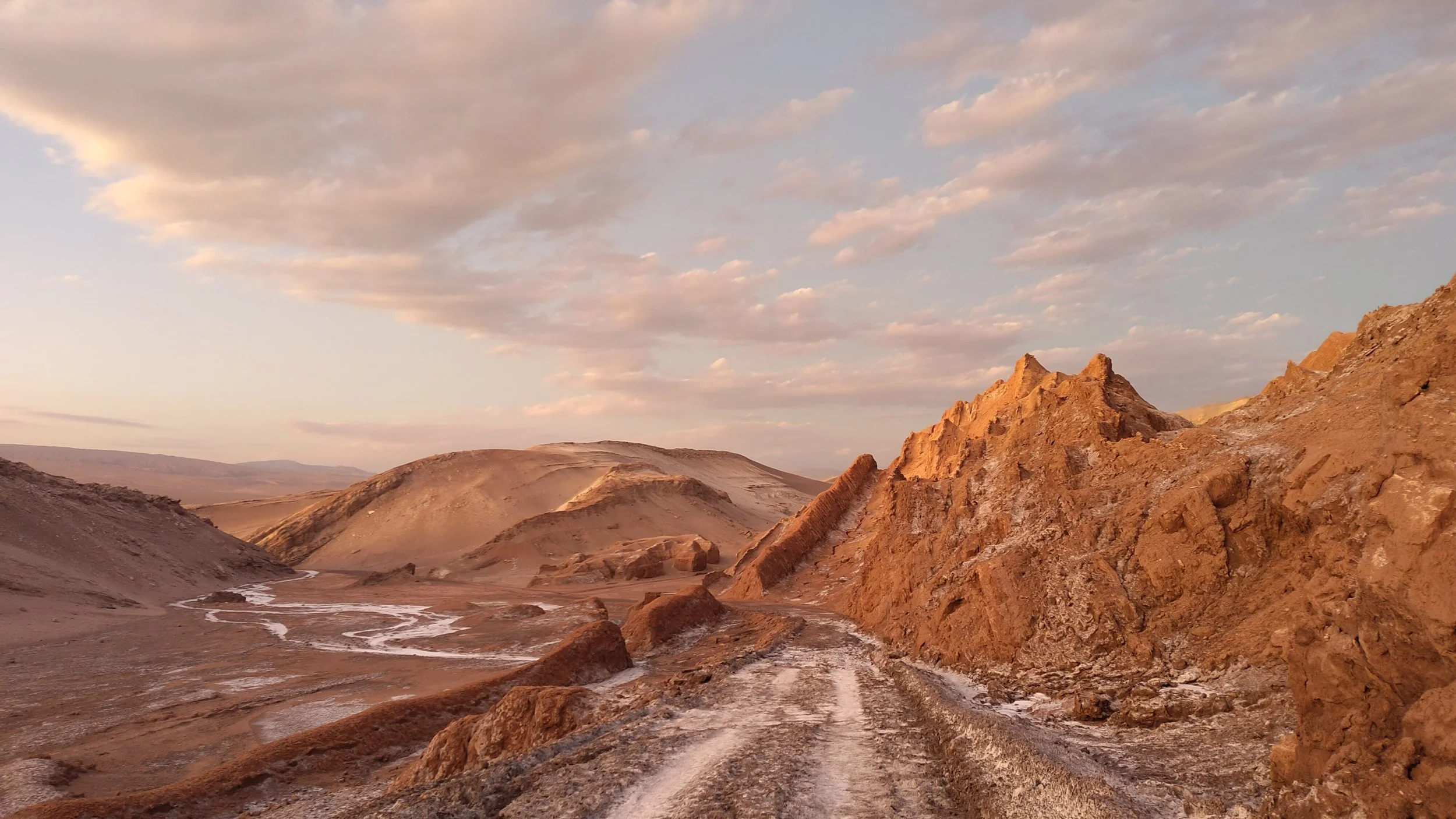 Berglandschaft mit roten Felsen und bewölktem Himmel bei Sonnenuntergang.