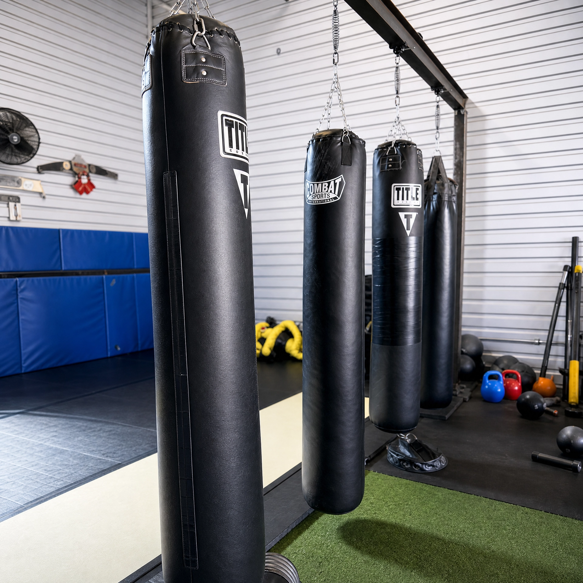 Black punching bag hanging in a gym, with other bags and fitness equipment in the background.