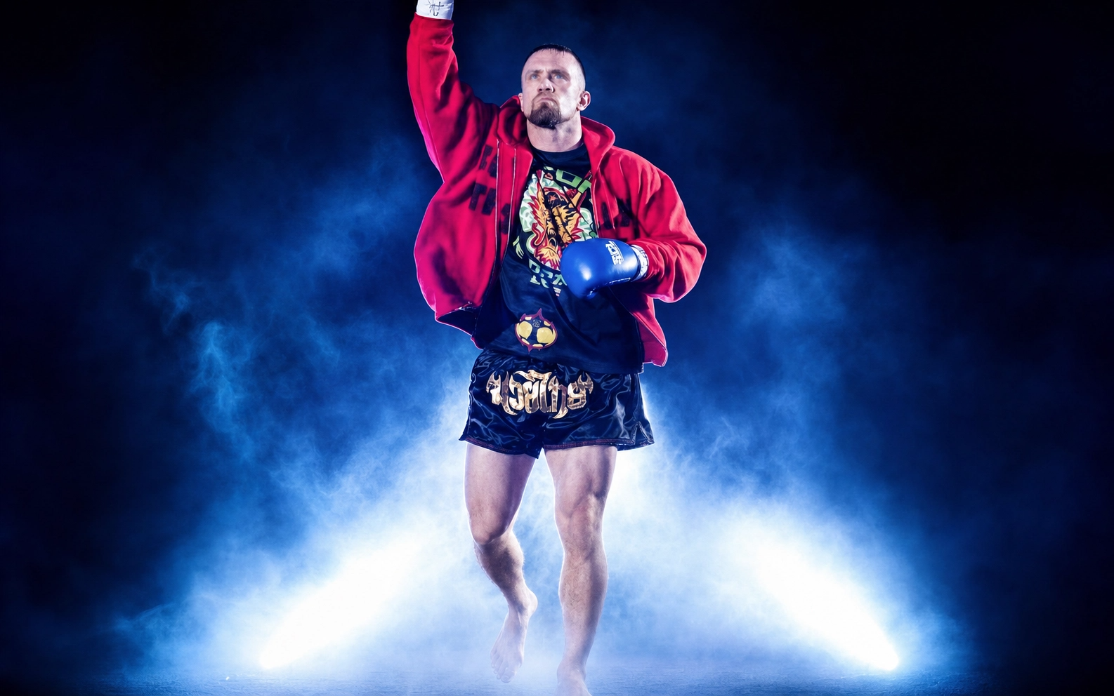 Muay Thai fighter walking towards the camera with one arm raised, wearing boxing gloves, shorts, a t-shirt with a tiger, and a red hoodie, surrounded by blue and white fog.