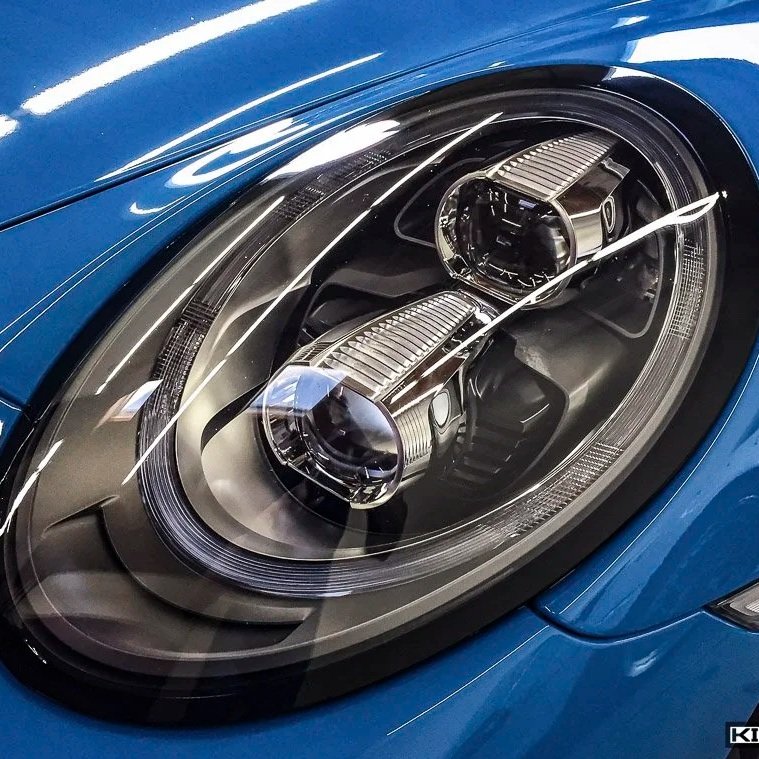 Close-up of a blue sports car's headlight with intricate detailing and reflections.