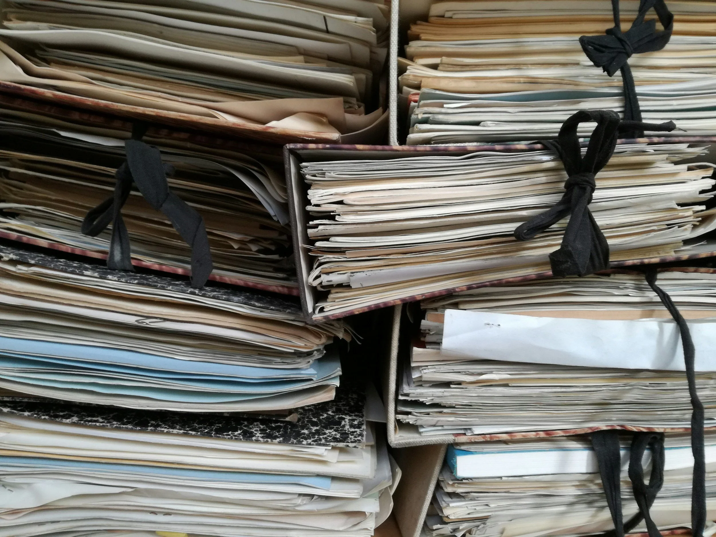Stacks of scattered papers and files organized in open-top cardboard boxes tied with black strings.