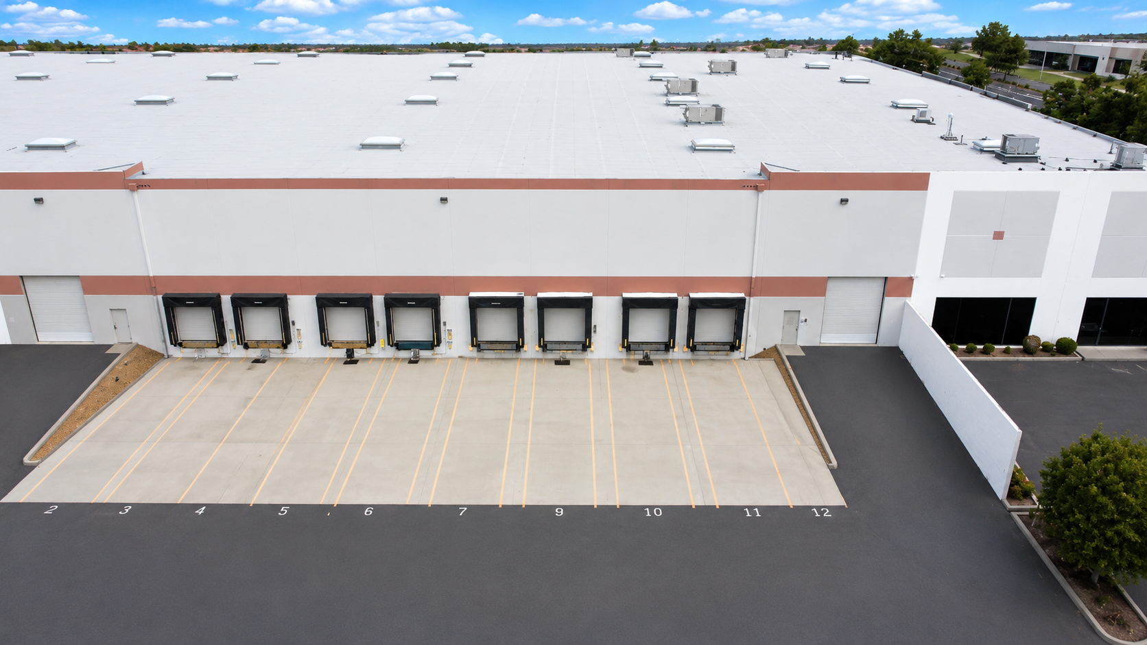 Aerial view of a large warehouse building with multiple loading docks and an empty parking lot in front.