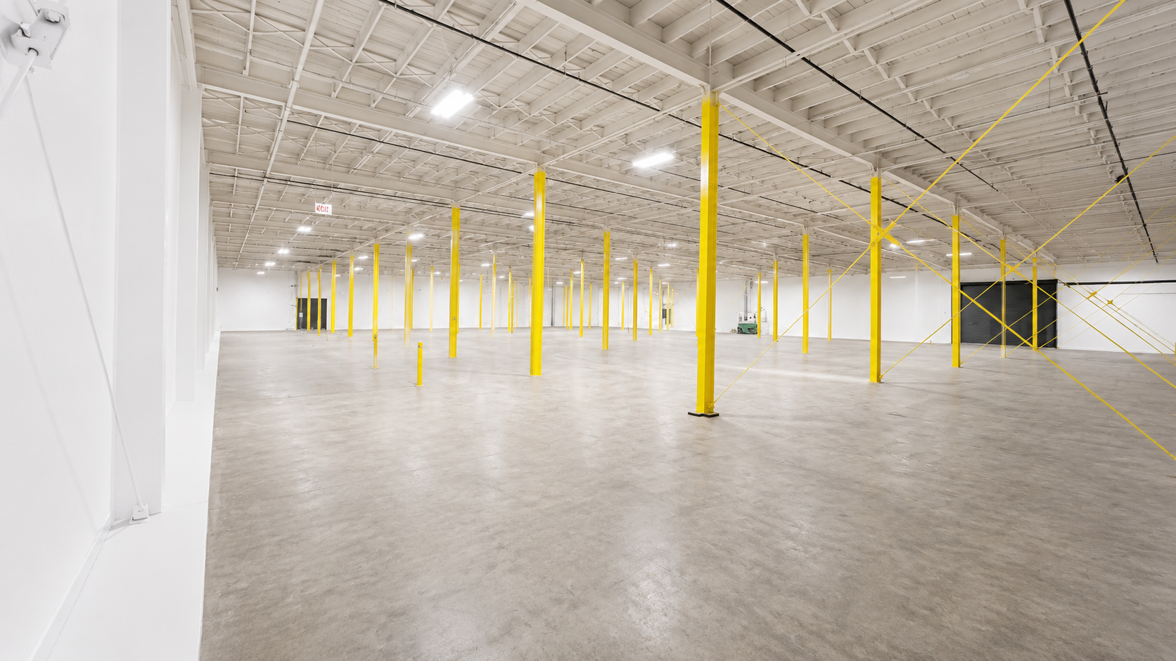 Empty warehouse with yellow safety poles and crossing yellow safety lines on the ceiling.