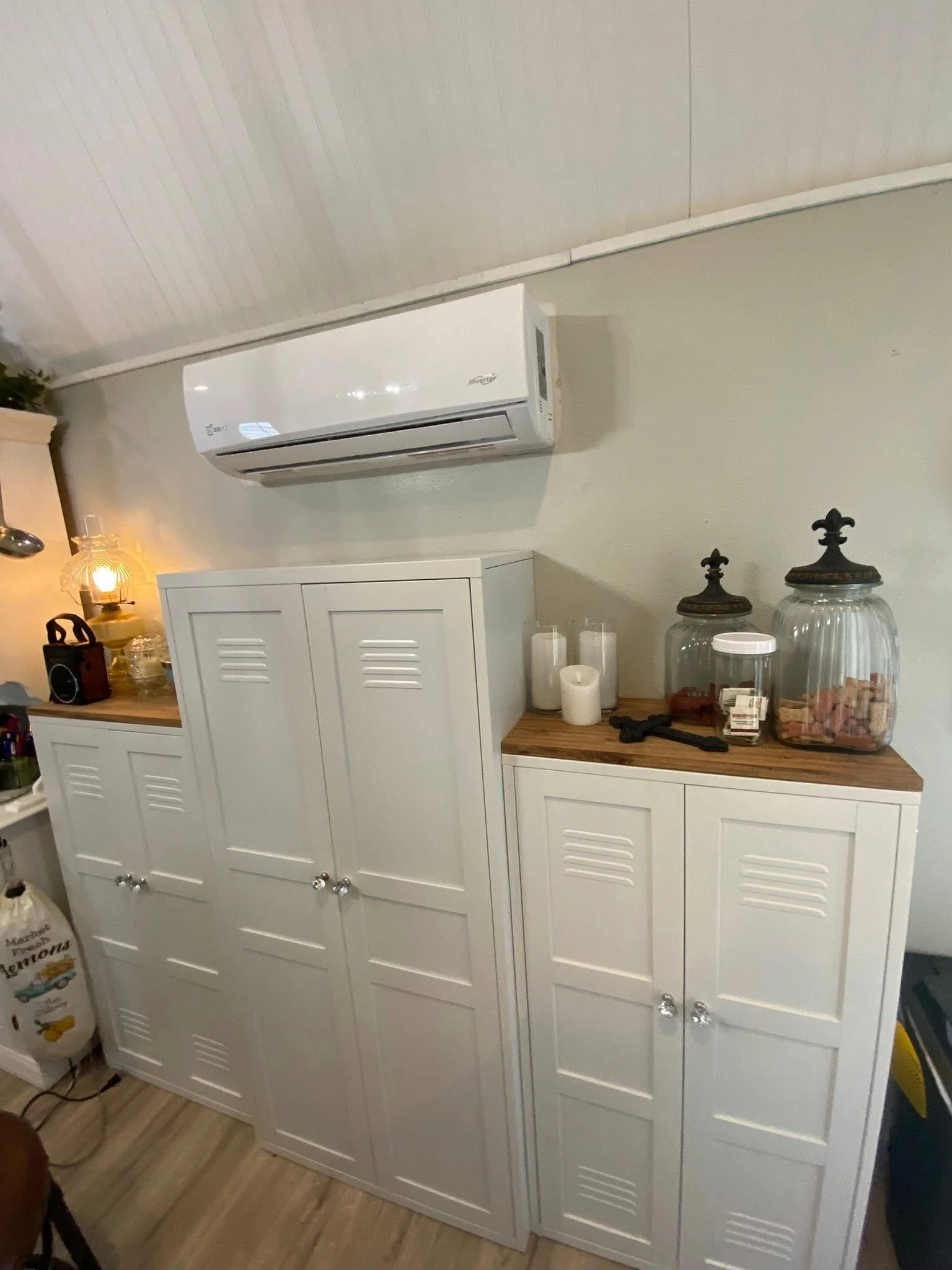 White kitchen cabinet with four doors and silver knobs, decorative jars, candles, a gun, and other small items on the wooden countertop.