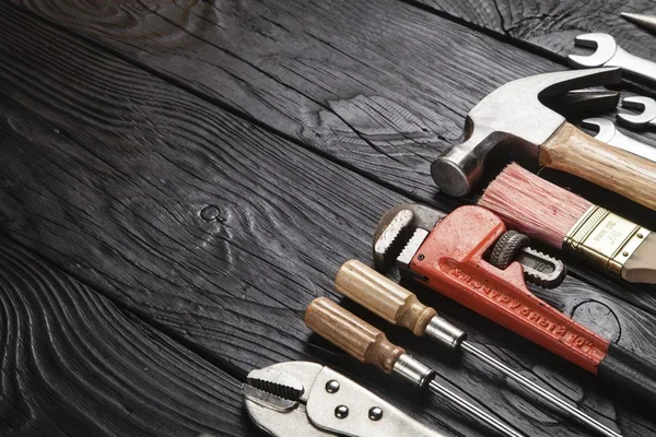 A collection of hand tools including a hammer, wrenches, screwdrivers, and a utility knife arranged on a dark wooden surface.