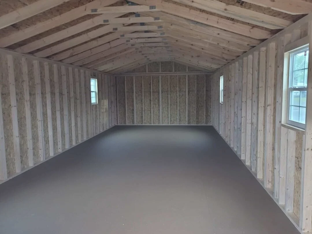 Interior of an unfinished room with exposed wooden framing, wood-paneled walls, a sloped ceiling, and three small windows.