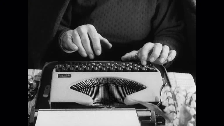 A person using a typewriter with a phone placed on top of it.