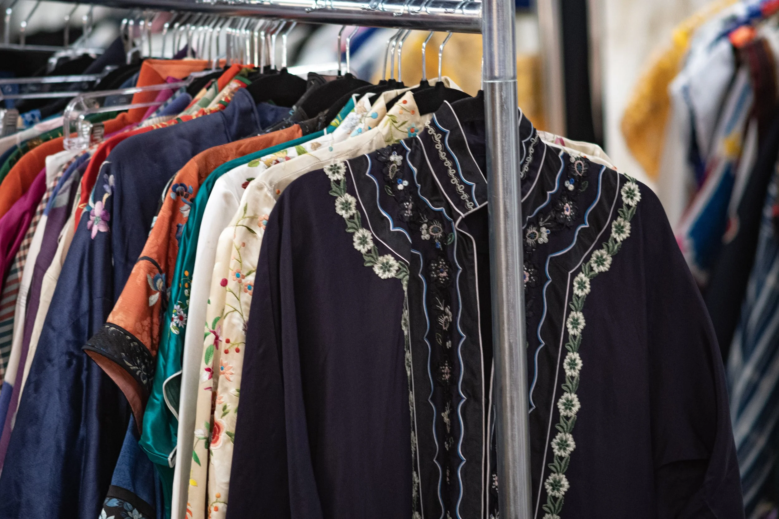 Clothing rack with a variety of colorful shirts and blouses, some with floral and embroidered designs.