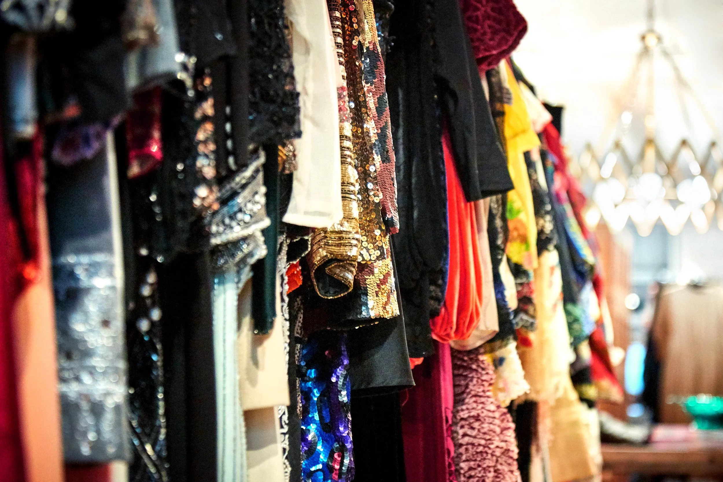 Rows of various fabric and clothing materials hanging on a rack, including sequined, patterned, and colorful textiles.