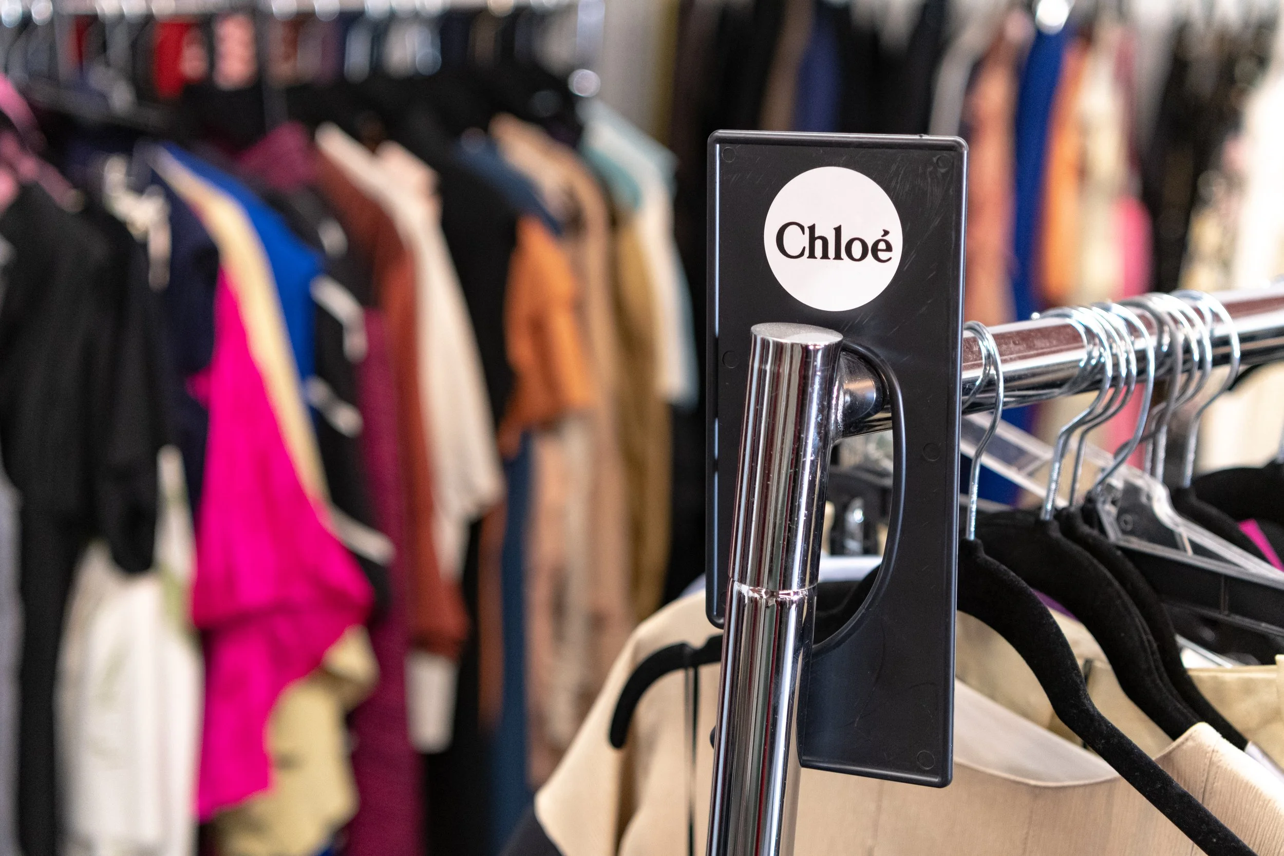 Clothing racks with various garments hang in a retail store, with a focus on the label 'Chloé' in the foreground.